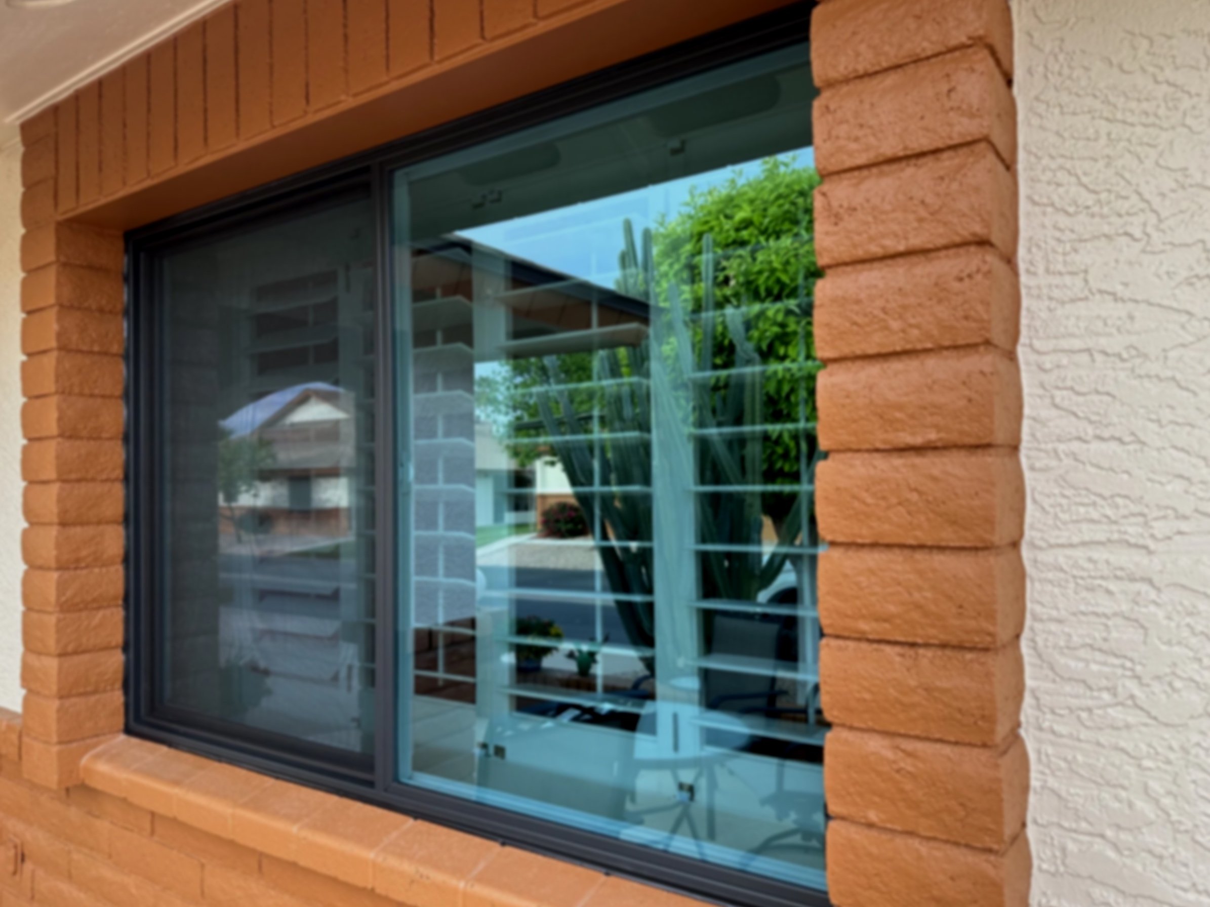 Reflective window with white blinds, brick wall, and view of trees and neighboring buildings.