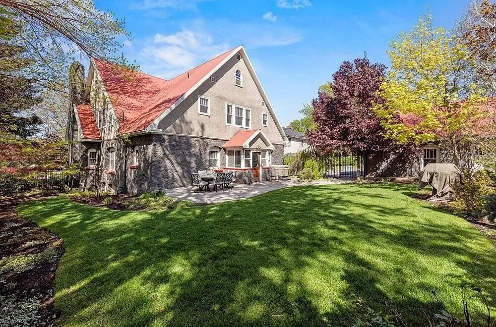Backyard of a house with a well-maintained lawn, trees with colorful leaves, and an outdoor patio with a dining table and chairs.