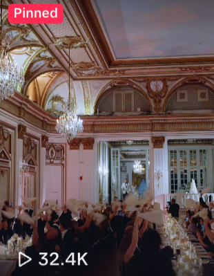 Elegant banquet hall with ornate gold trim, large chandelier, high ceilings, and a long table with guests dining.