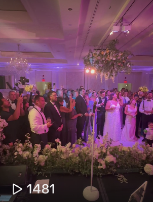 People attending a wedding reception, dancing and socializing in a decorated banquet hall with chandeliers and floral arrangements.