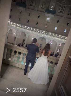 A newlywed couple standing on a balcony overlooking a courtyard with string lights, surrounded by an elegant stone building at night.