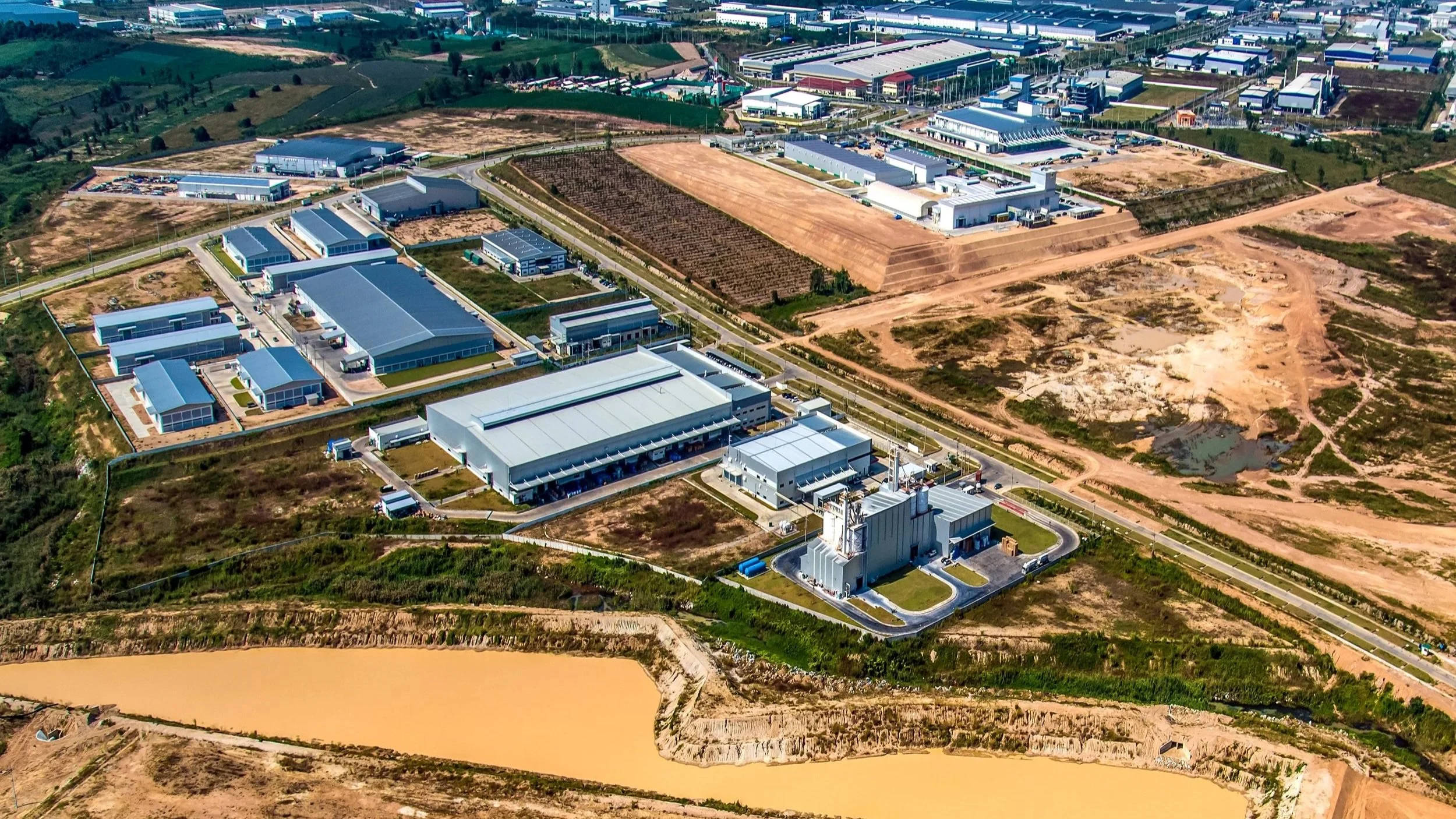A digital twin aerial view by deepskyiq of an industrial area with multiple large buildings, warehouses, roads, and construction sites, along with a body of water in the foreground.