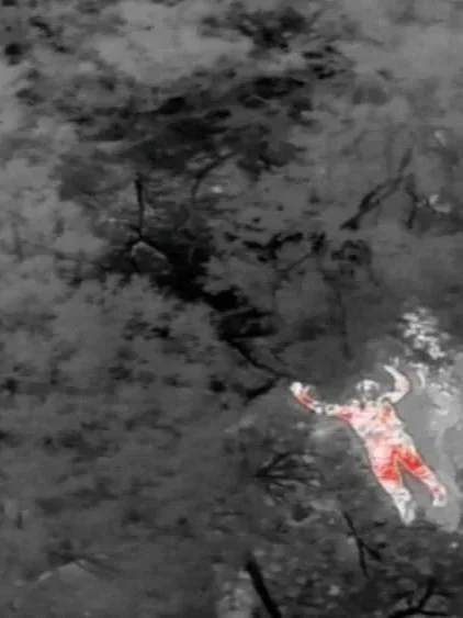 A person was detected by a security drone using DeepSky IQ's Protect drones' thermal imaging, and AI detection, caught lying on the ground near water, with tree branches overhead.