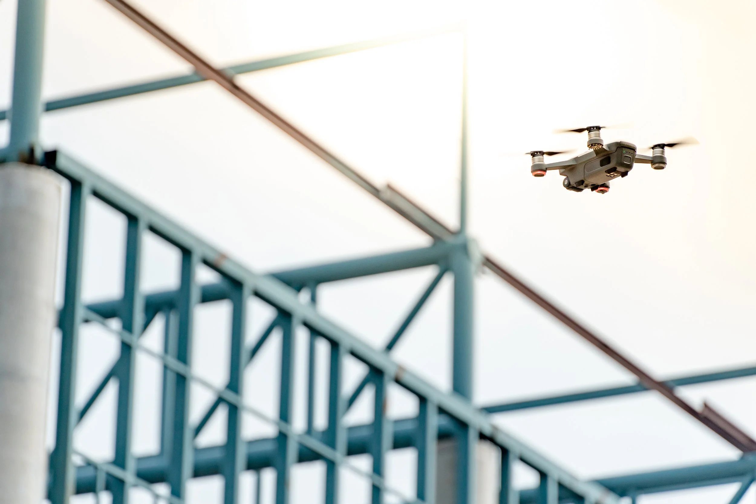 A drone flying in the sky near a blue metal structure.