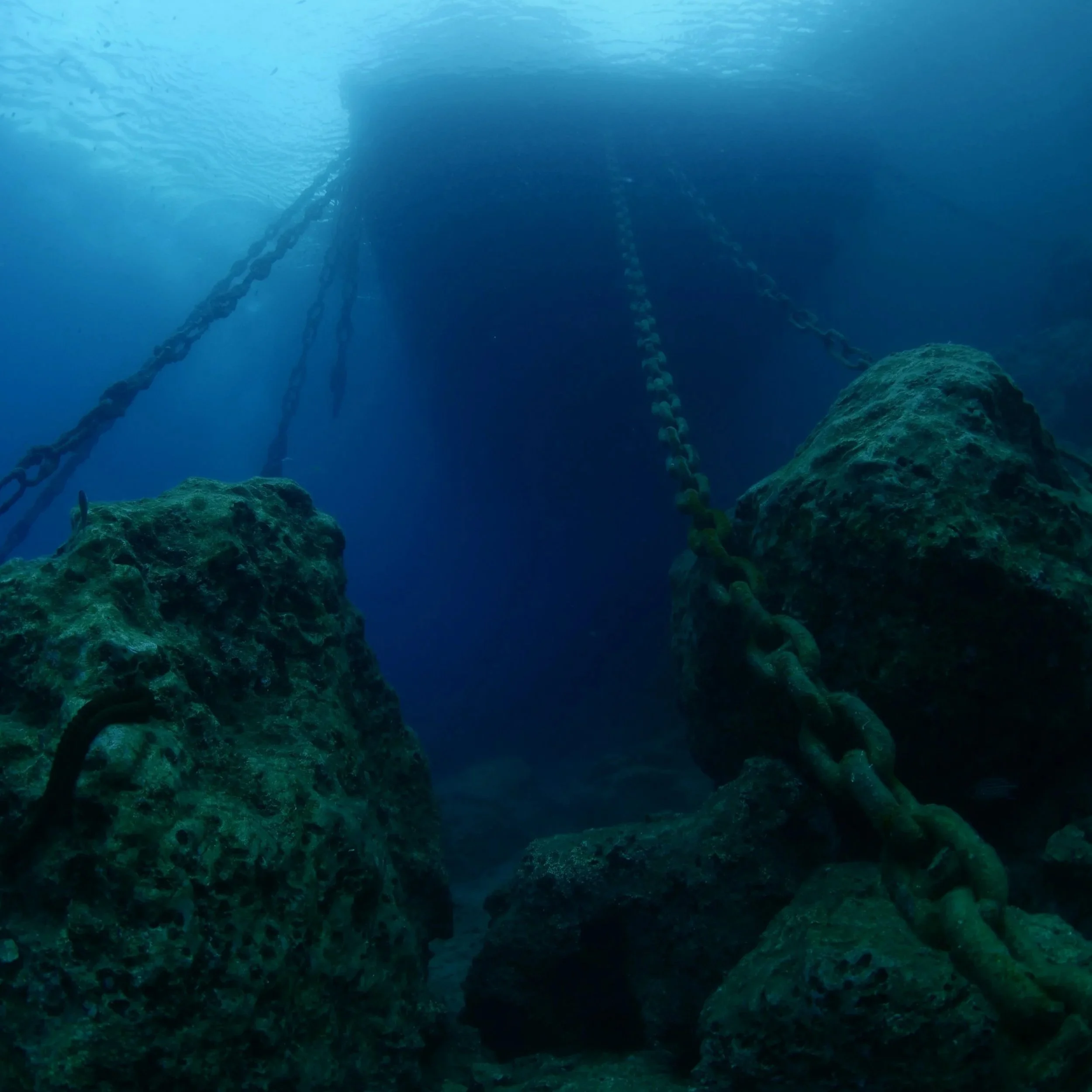 Underwater ROV inspection by DeepSky IQ of chains attached to a marina platform, with a blue ocean background and sunlight filtering through the water.