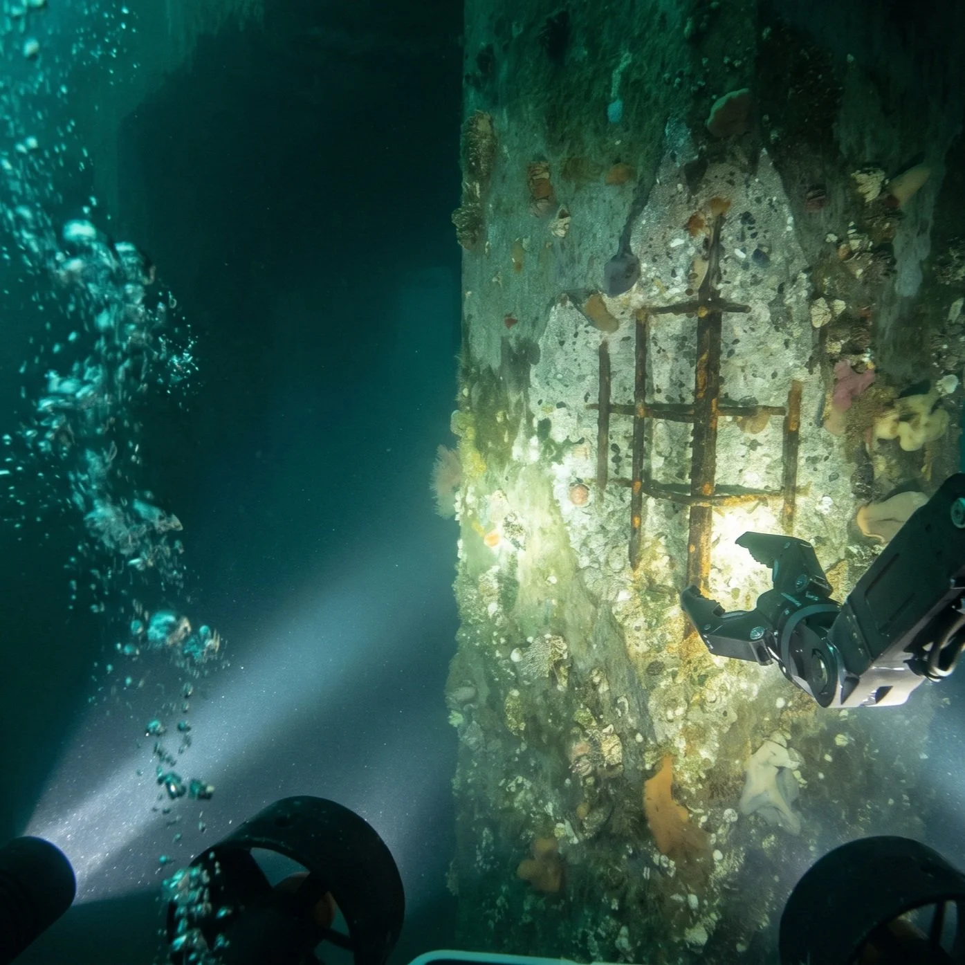 Underwater ROV scene inspecting a submerged or sunken structure, surrounded by coral and marine life, with obvious defects as viewed through an ROV with lights by DeepSky IQ.
