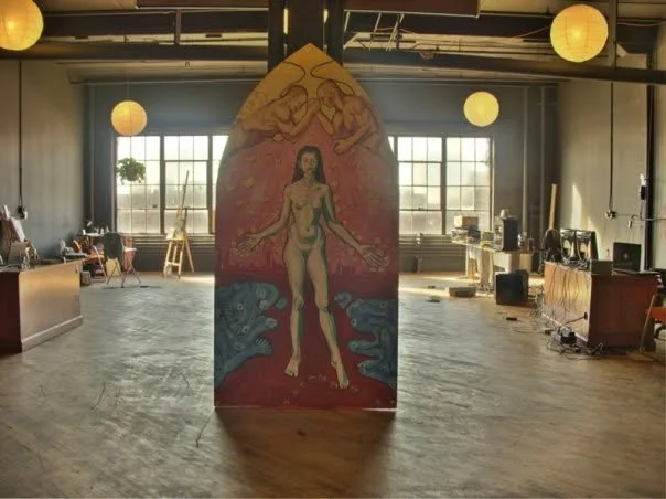 Painted panel in an open studio with easels and large windows
