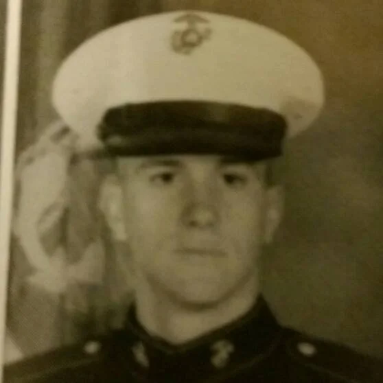 Black and white photo of a young man in a US Marine Corps dress uniform and a white cap.