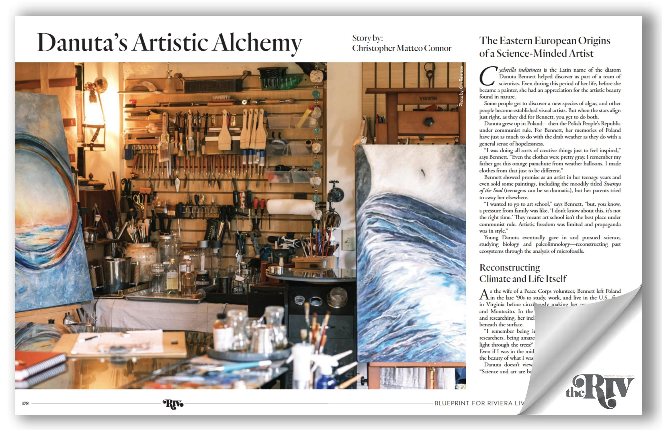 An artist's studio filled with painting supplies, including brushes, jars, and paintings on the walls, with the focus on a work-in-progress landscape painting of a wave.