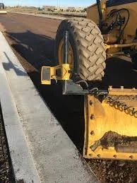 Close-up of a yellow street sweeper or road maintenance machine on a paved road.