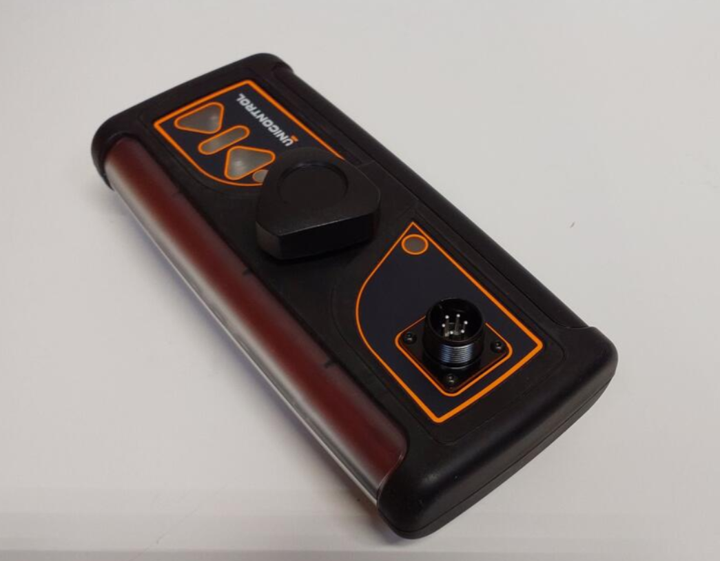 A black and brown medical device with a circular connector port and a black switch or button, positioned on a white surface.