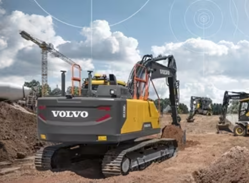 A yellow and black Volvo excavator at a construction site with other equipment and a crane in the background, under a partly cloudy sky.