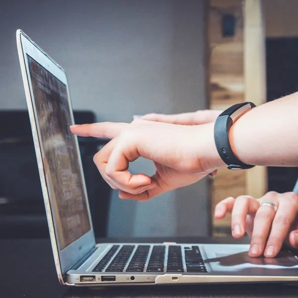 Person using a laptop with one finger pointing at the screen, wearing a black wristband.