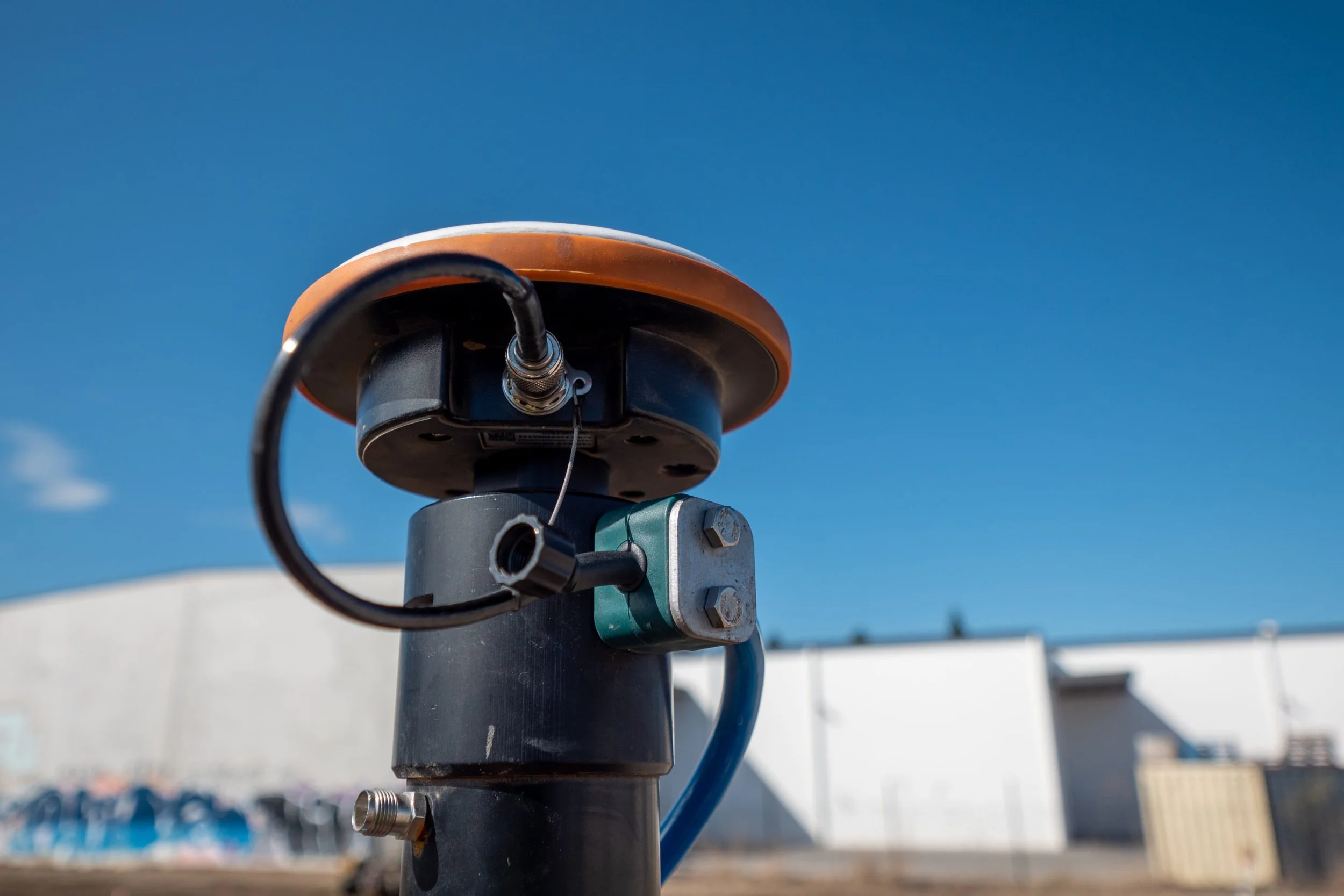 Close-up of a black outdoor security or surveillance camera mounted on a pole against a clear blue sky.