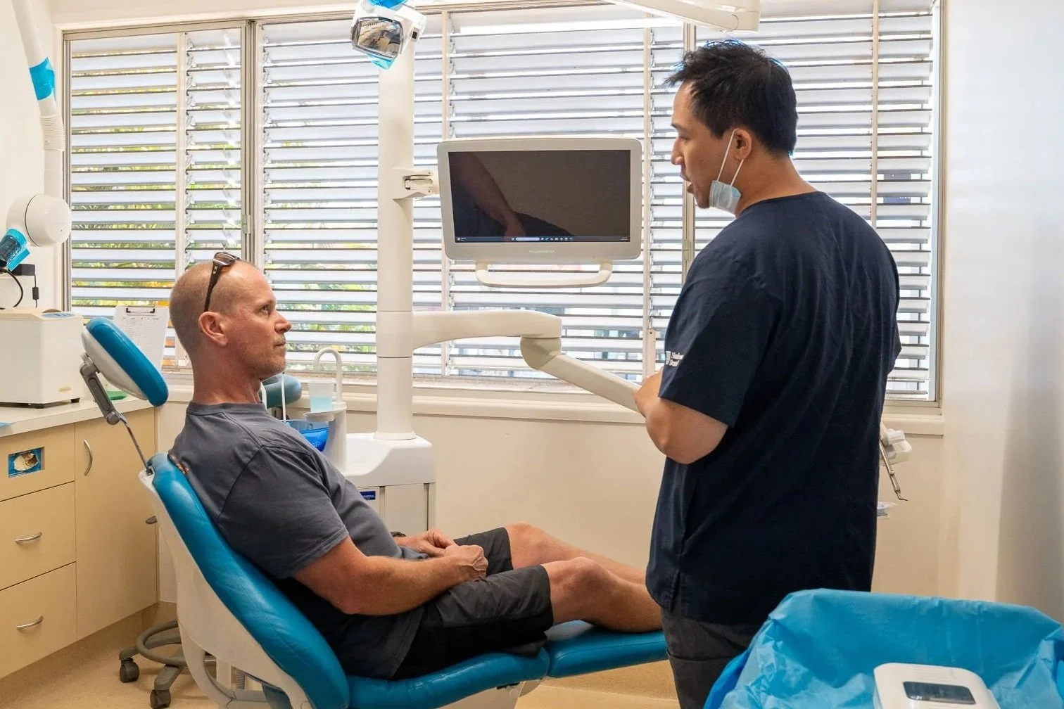 Close-up of a dental cleaning procedure with a person receiving treatment; dental tools are used near the person's open mouth, revealing teeth and gums.