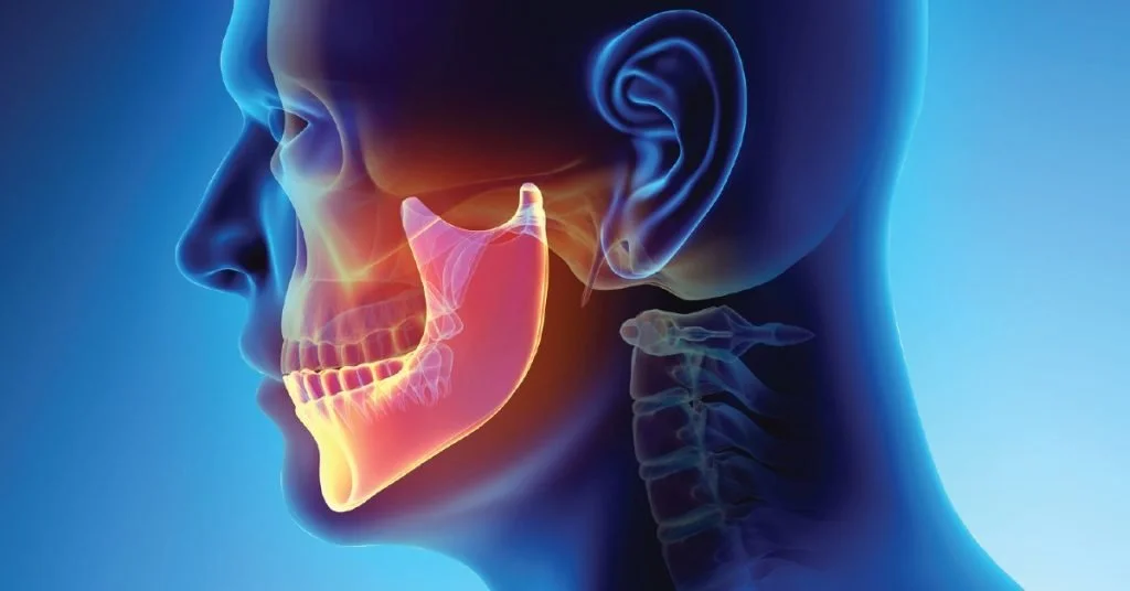 Woman in a yellow sweater experiencing tooth pain or discomfort, holding her cheek with a pained expression in a bright living room.