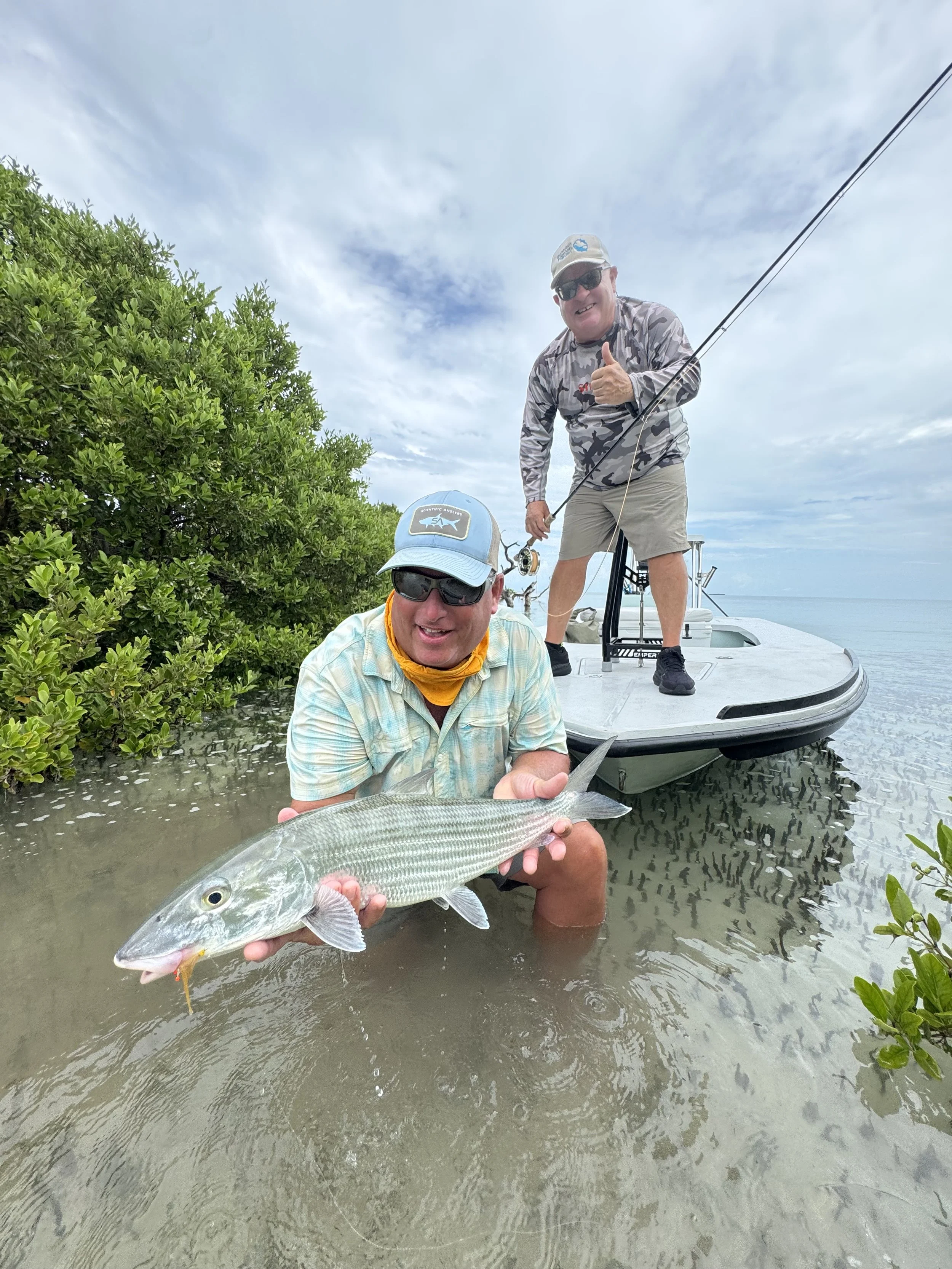 Angler holding a bonefish beside a flats skiff in a mangrove creek in Grand Bahama.