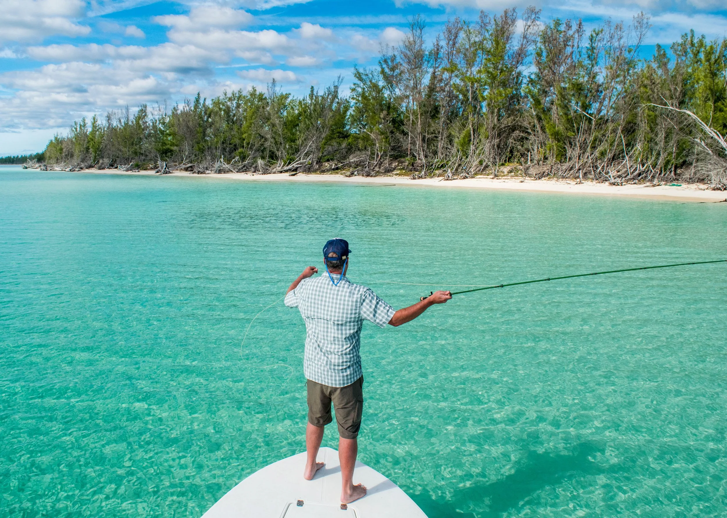 Angler casting from the bow of a flats skiff to a large school of bonefish across a turquoise flat in Grand Bahama.