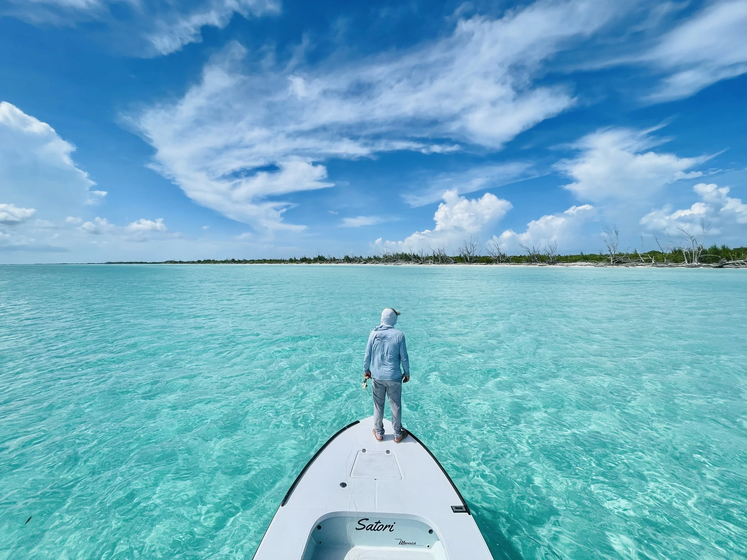 Angler casting from the bow of a flats skiff across a clear white-sand flat in Grand Bahama.