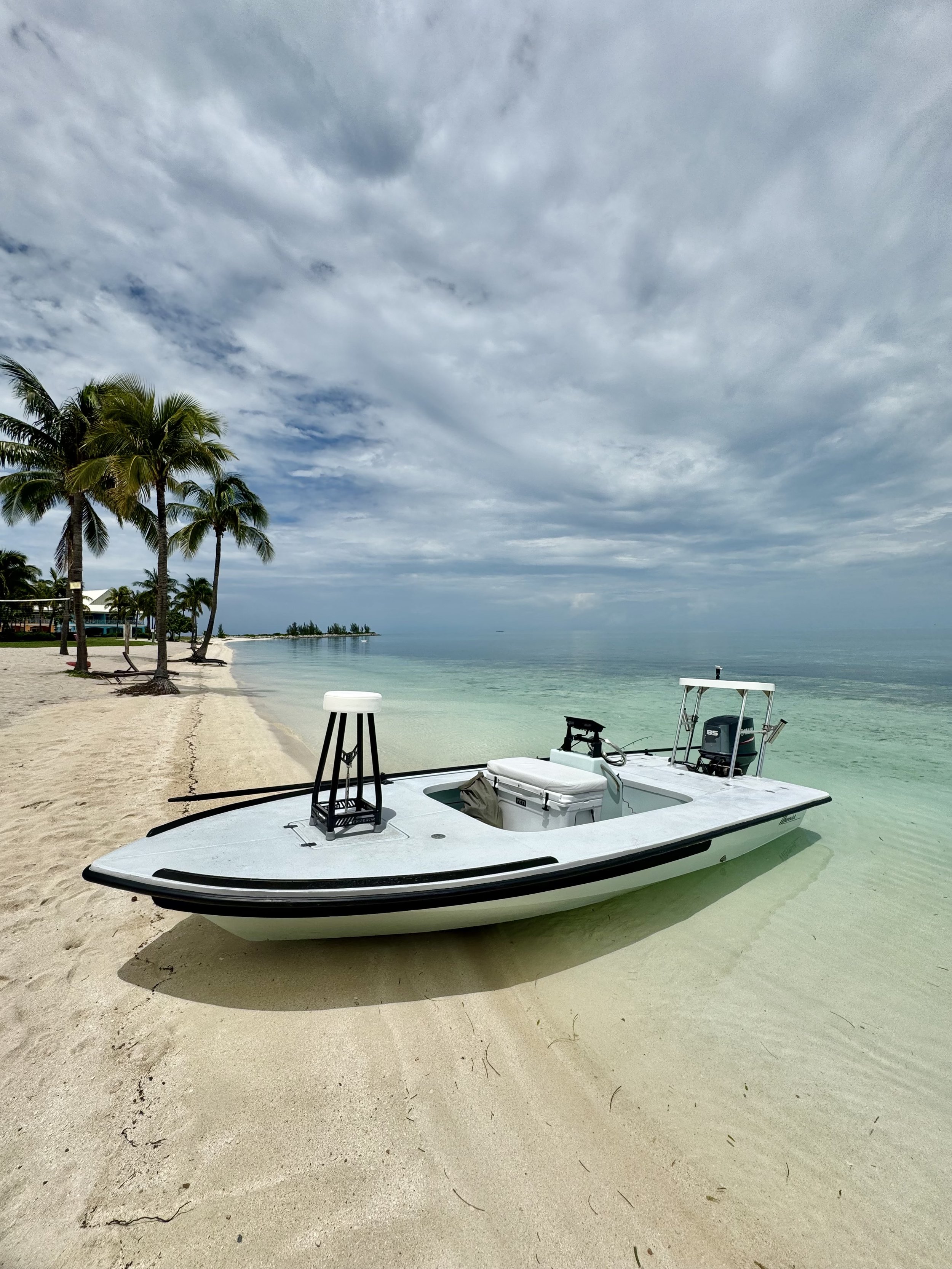 Goombay Outfitters flats fishing boat on a sand beach in The Bahamas, equipped for shallow-water fishing adventures.