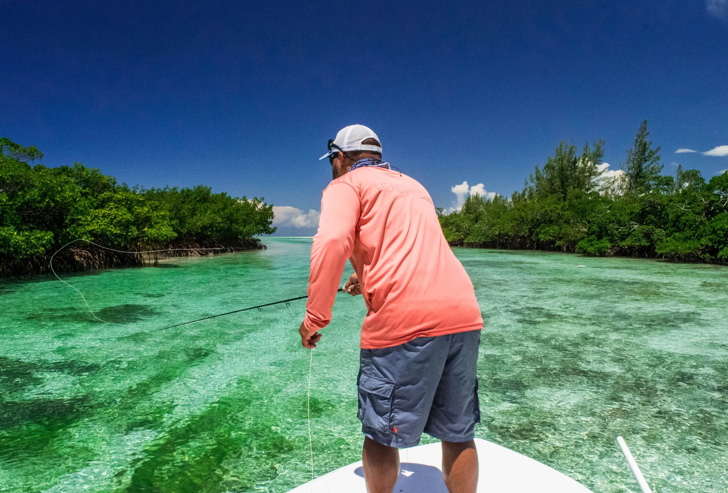 Angler on the bow of a flats skiff serching for bonefish in shallow flats of Grand Bahama, Bahamas.
