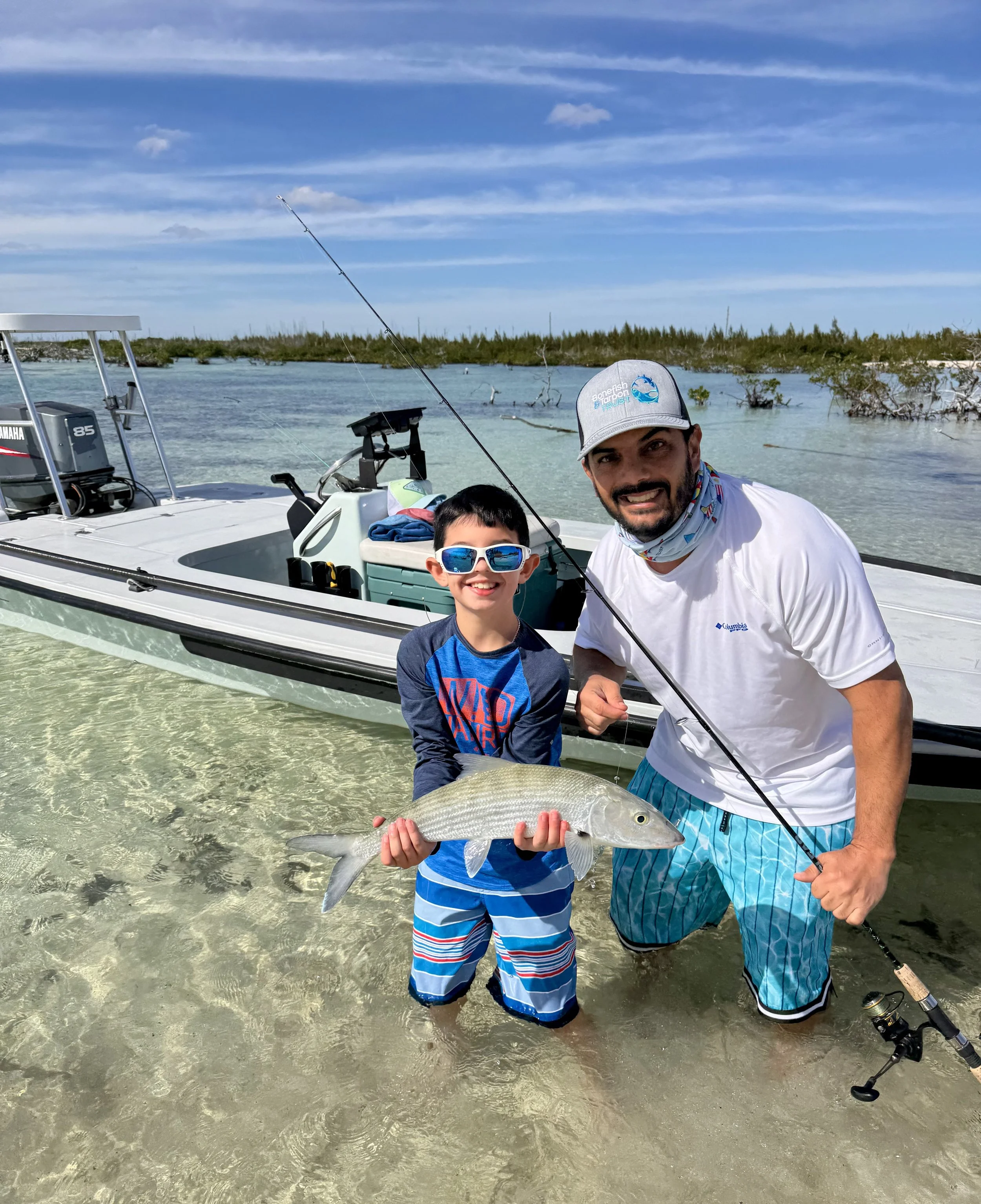 Young angler and proud father posing with a bonefish beside a flats skiff in Grand Bahama.