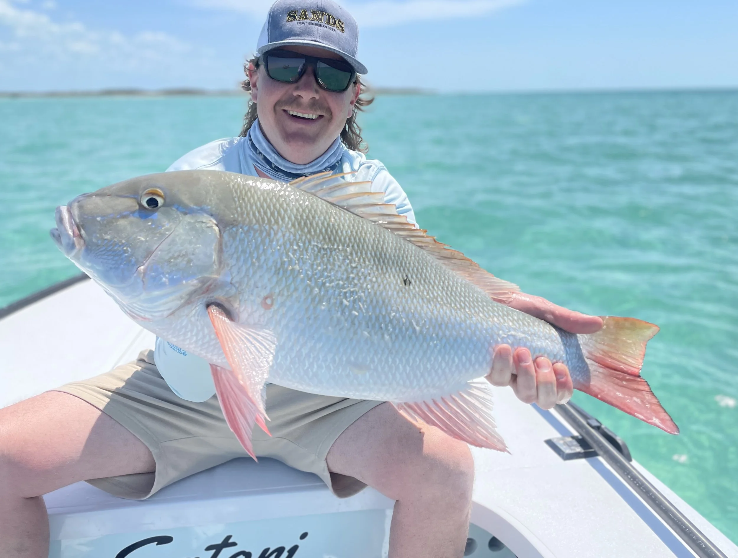 Angler holding a large mutton snapper aboard a flats skiff in Grand Bahama, Bahamas.