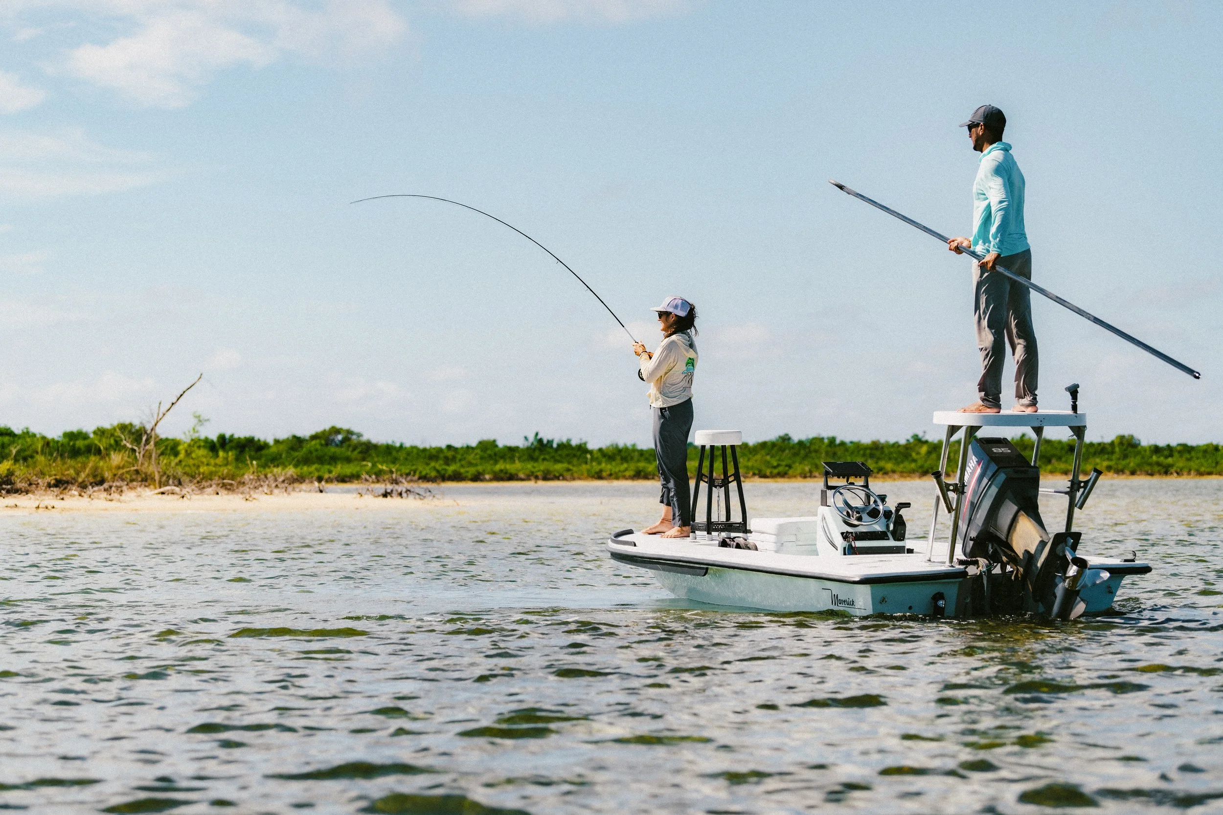 Angler fighting a bonefish from a flats skiff while a guide poles across the shallow waters of Grand Bahama.