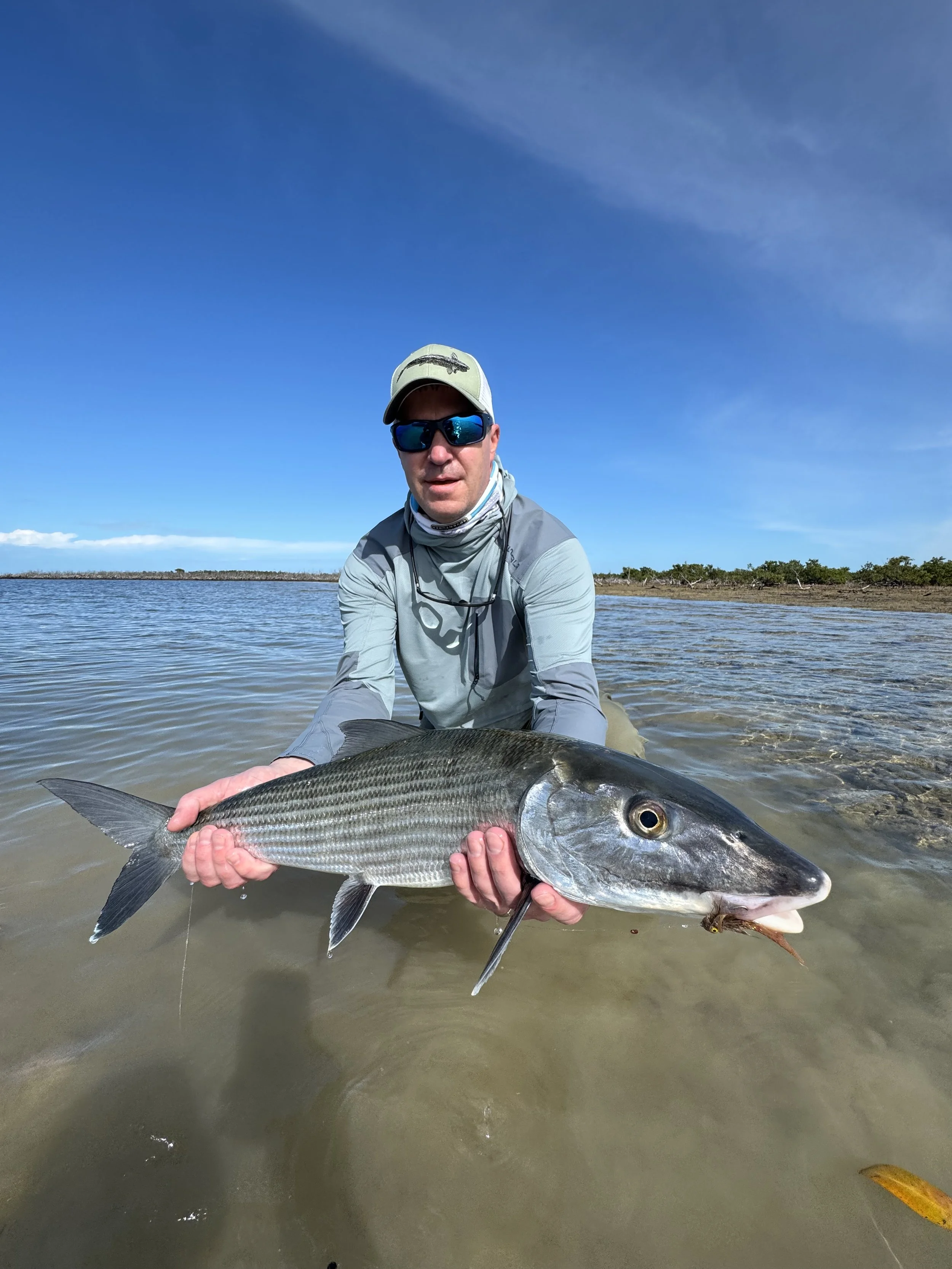 Angler holding a trophy bonefish while fly fishing shallow flat in Grand Bahama, Bahamas.