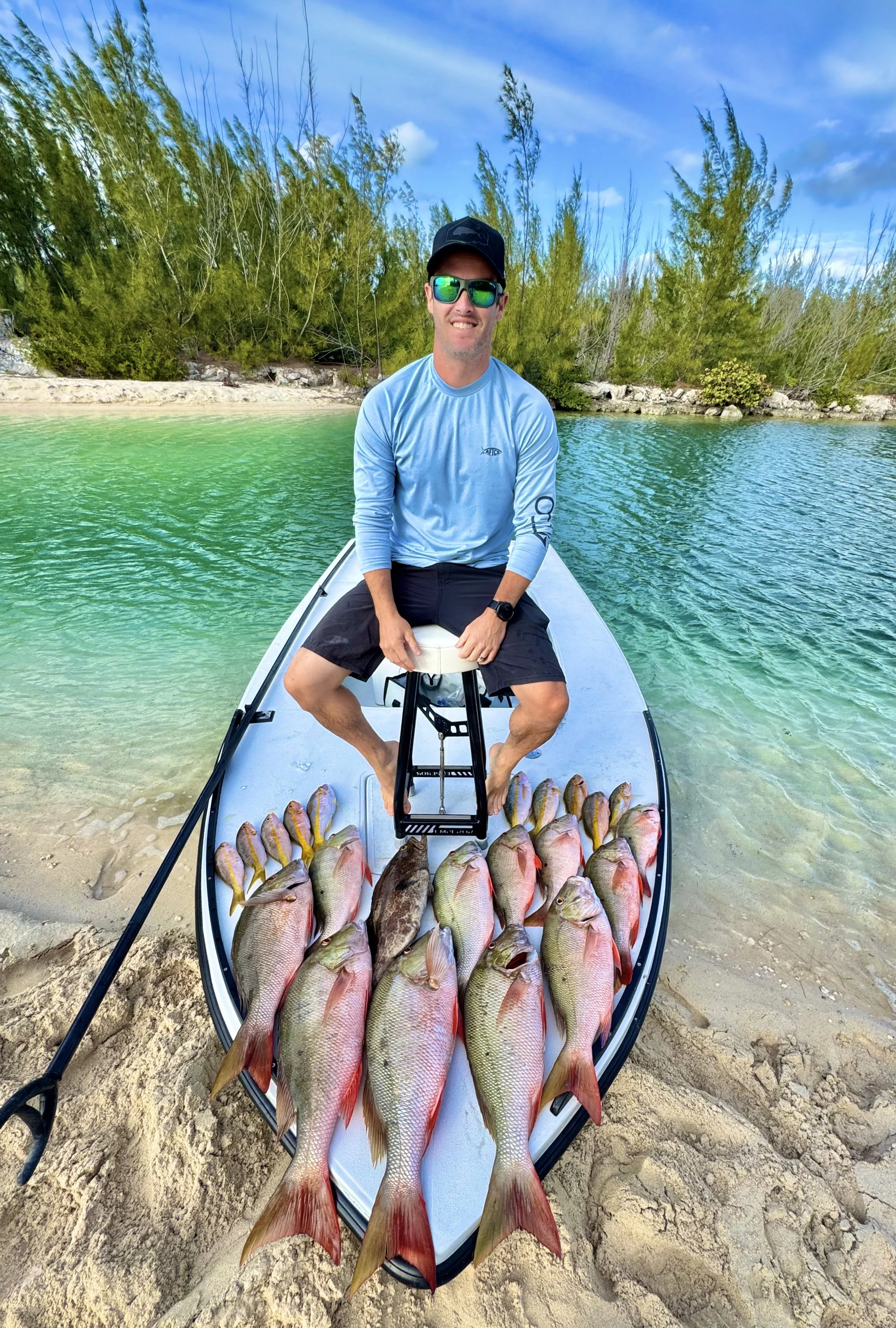 Angler sitting on a flats skiff with a mixed catch of mutton snapper and reef fish in the shallow waters of Grand Bahama.