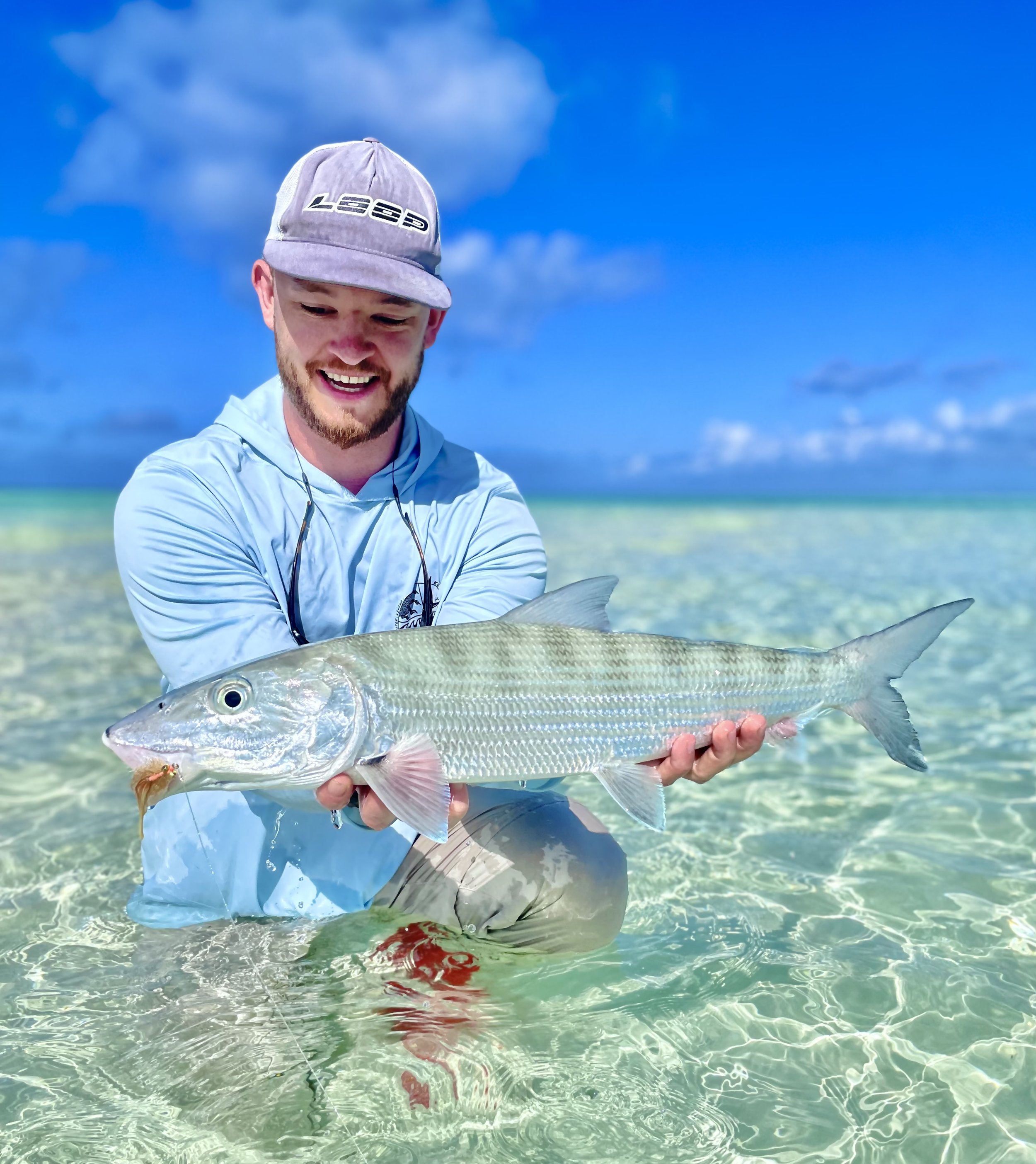 Angler holding a large bonefish while wading on a shallow clear-water flat in Grand Bahama, The Bahamas.