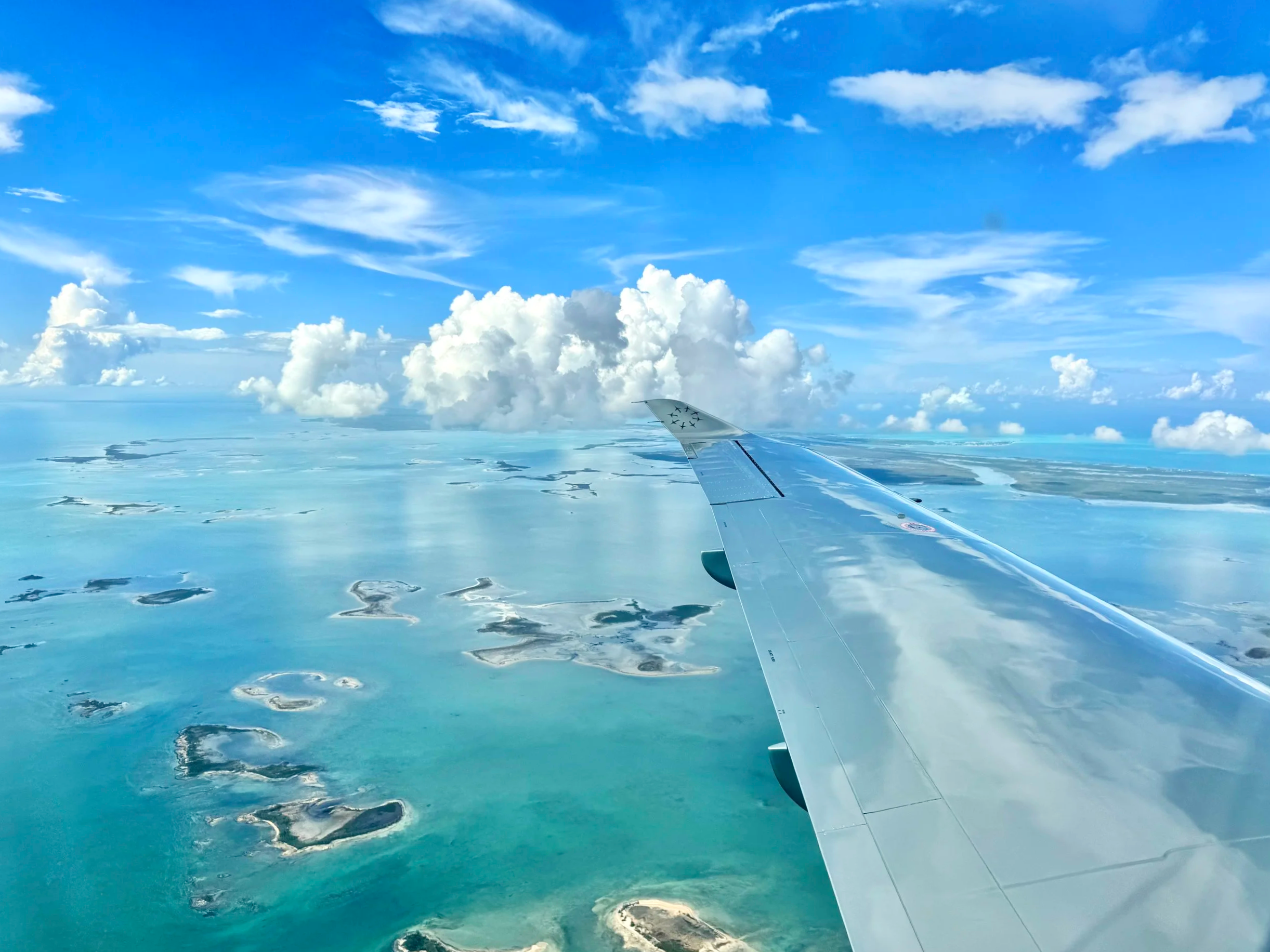 View from an airplane window showing wing and a vast landscape of water and land beneath a partly cloudy sky.