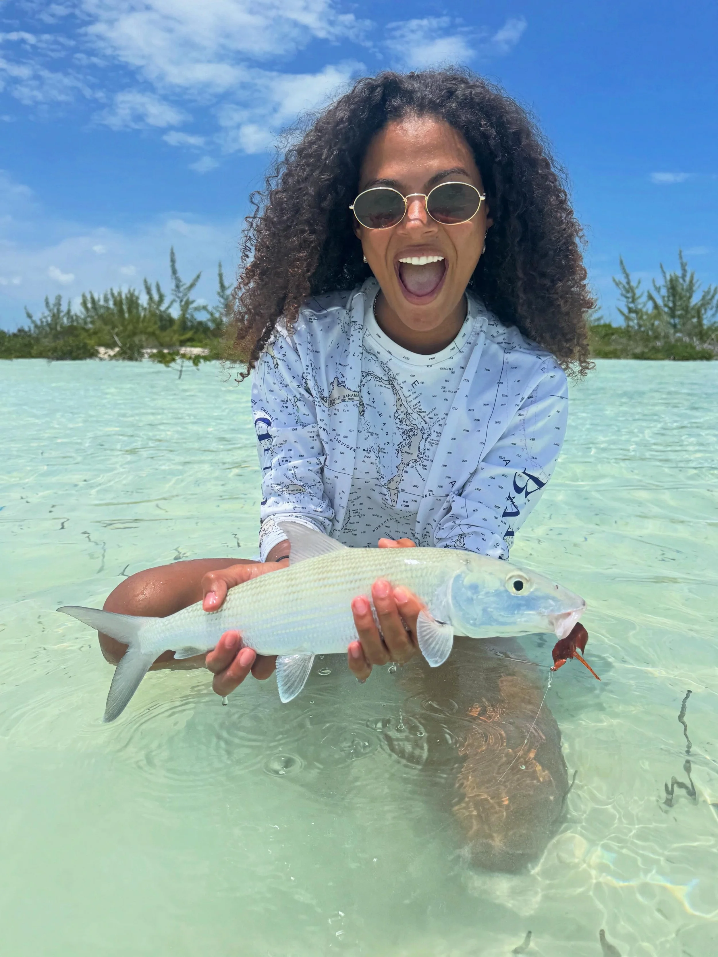 Angler holding a bonefish while wading a shallow white-sand flat in Grand Bahama.