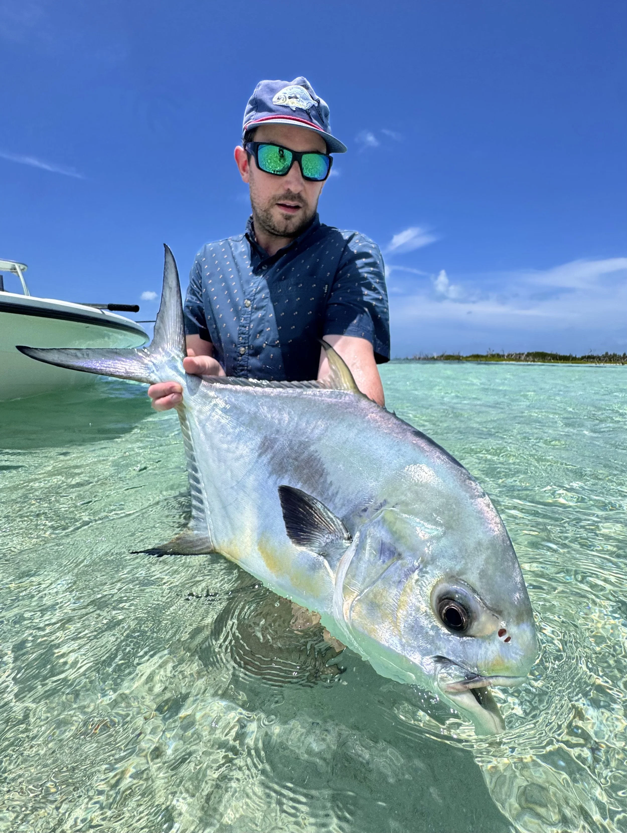 Angler holding a permit while wading beside a flats boat in shallow water in Grand Bahama.