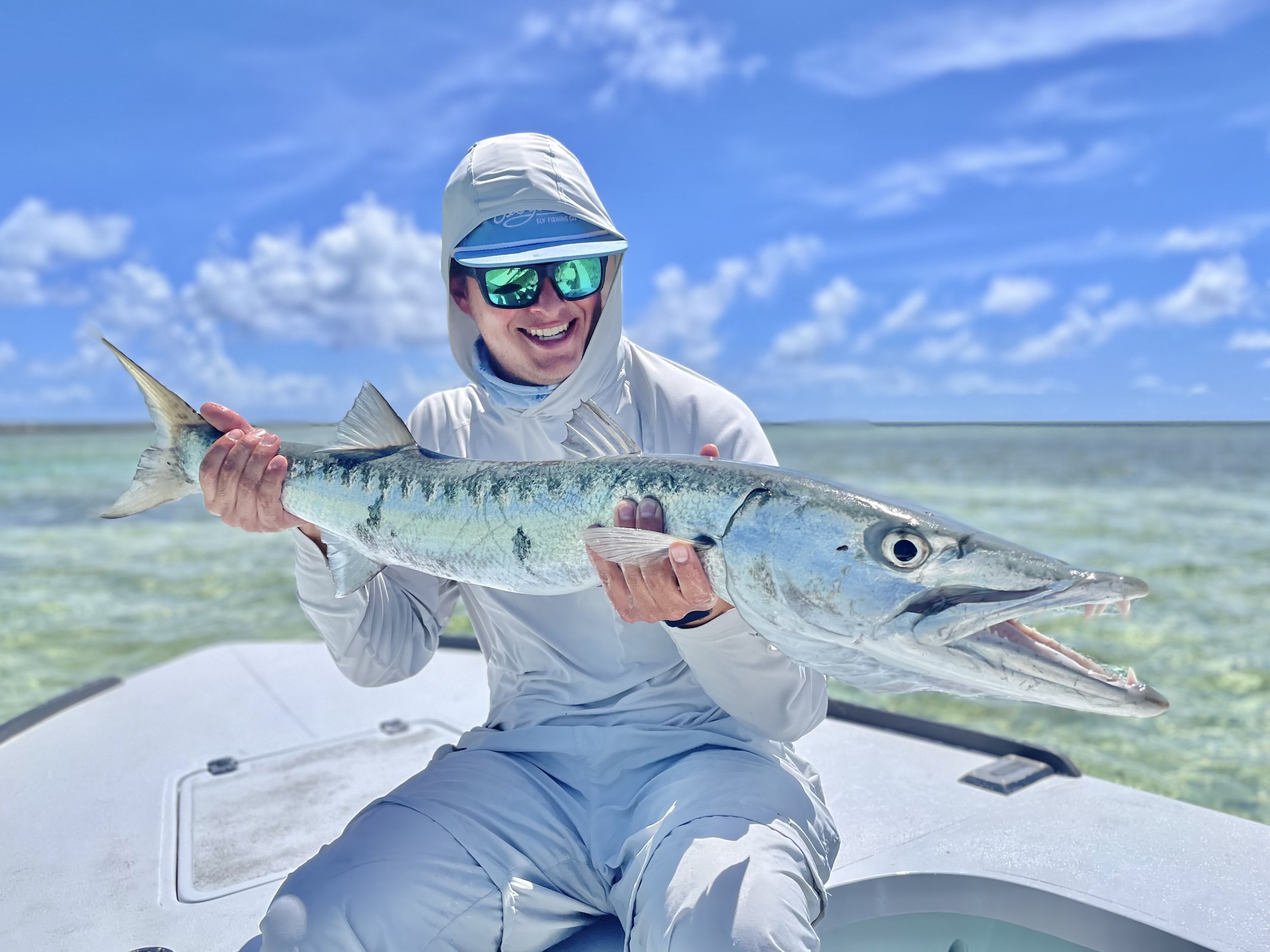 Angler holding a barracuda aboard a flats skiff in Grand Bahama, Bahamas.