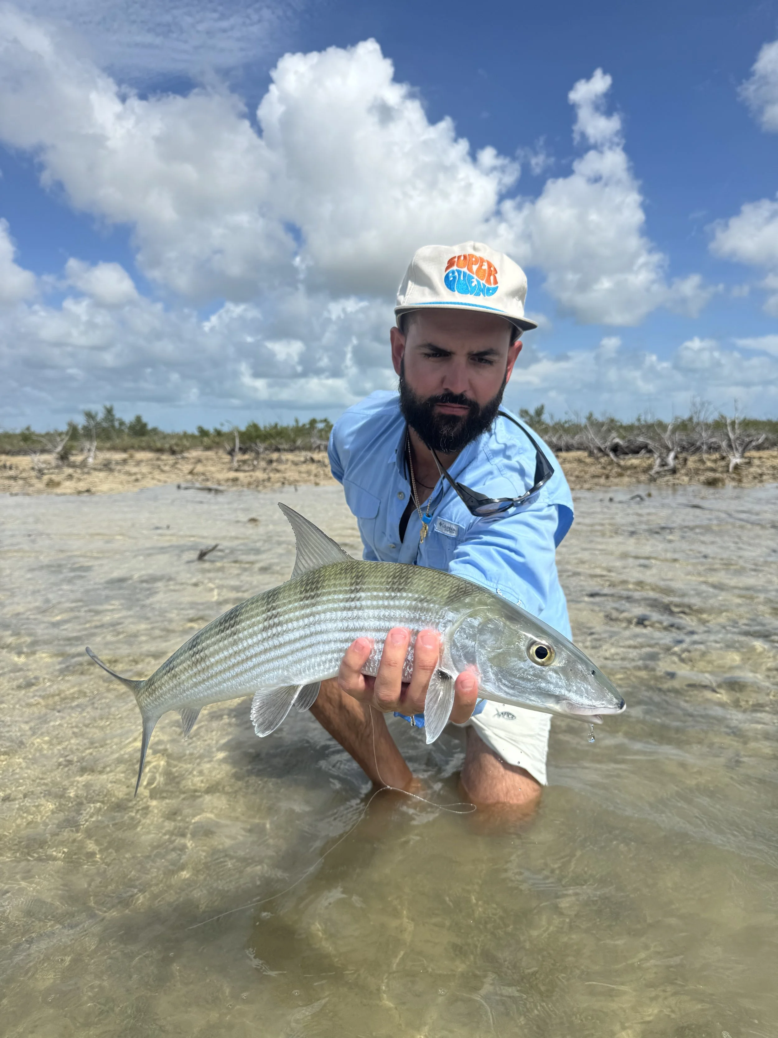 Angler holding a bonefish while wading a shallow flat in Grand Bahama, Bahamas.