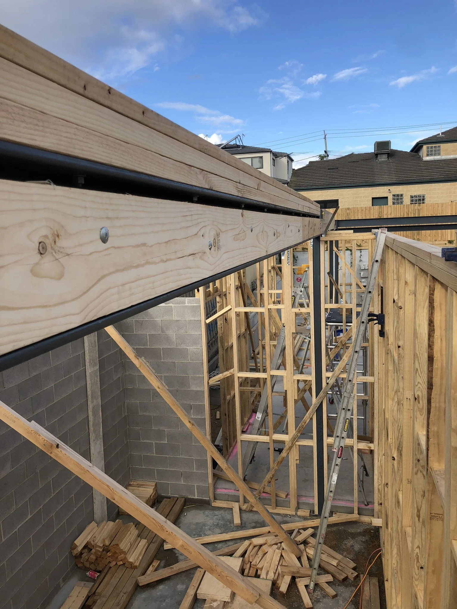 Construction site with wooden framing, scaffolding, and tools in progress beneath a blue sky with a few clouds.
