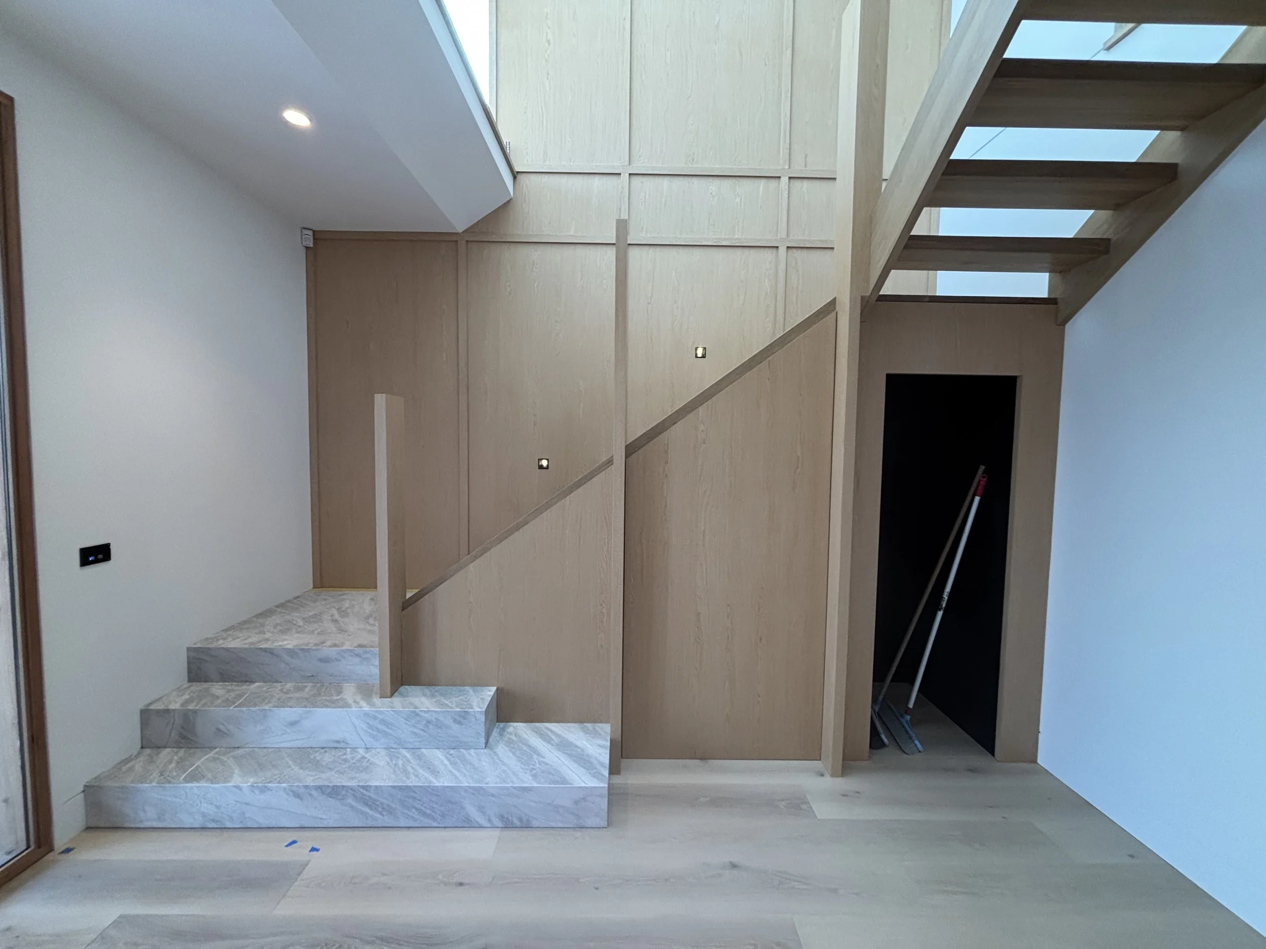 Modern interior entrance with marble stairs leading to a new open space, wood-paneled wall on the right, and light hardwood flooring.