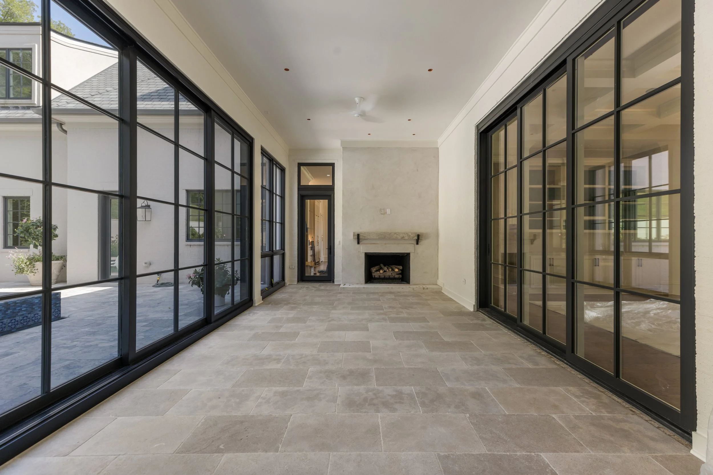 Room with large black-framed windows, a fireplace, tiled floor, and a white ceiling with small recessed lights.