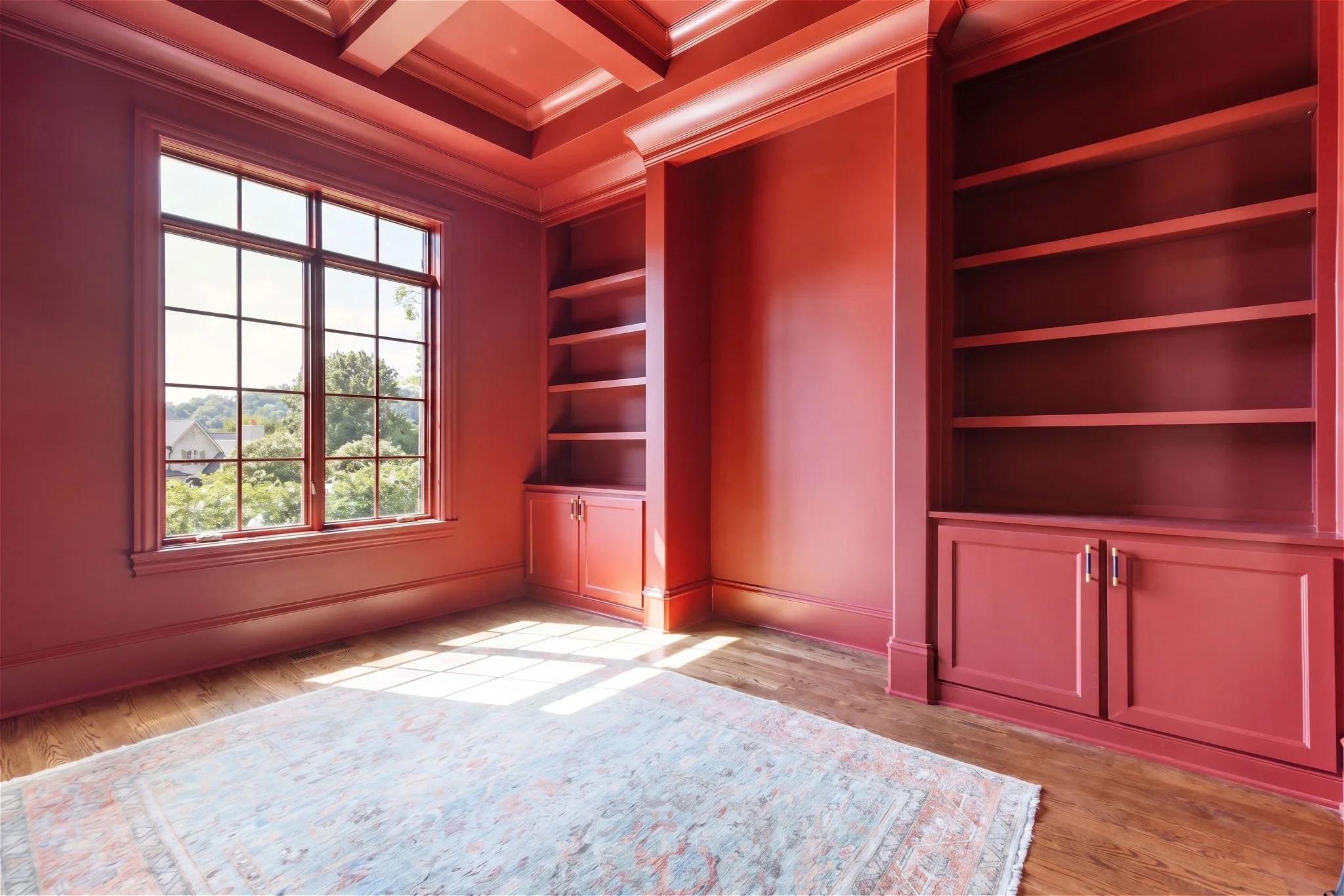 Sunlit room with large window, pink walls, built-in pink bookshelves, light hardwood floors, and a patterned area rug.