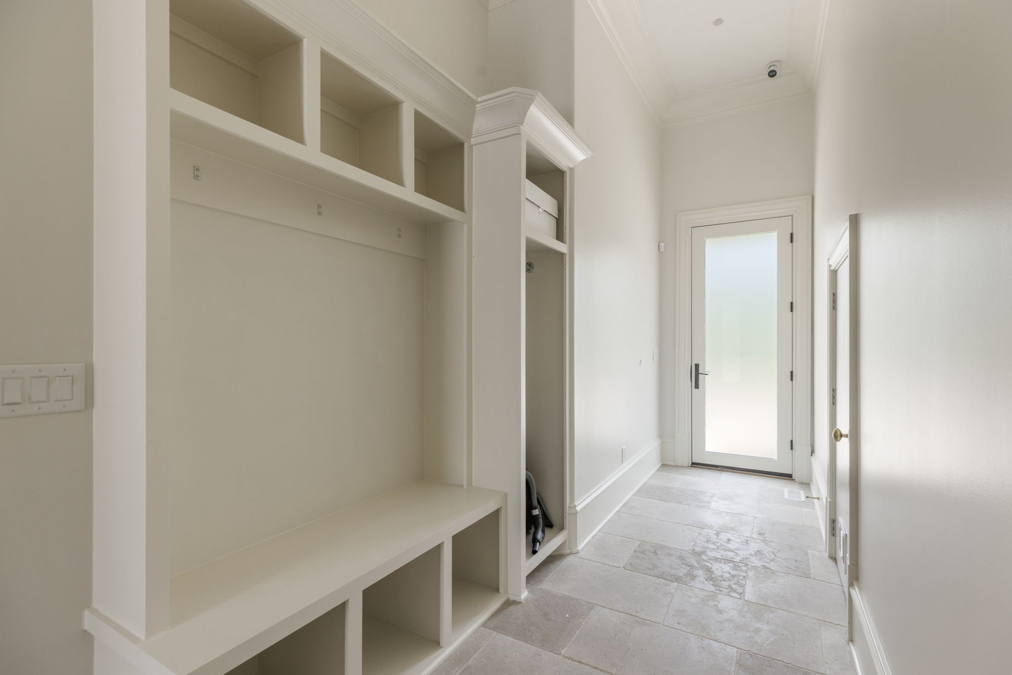 Mudroom with white built-in shelves and a glass door leading outside, light-colored limestone flooring, and white walls.