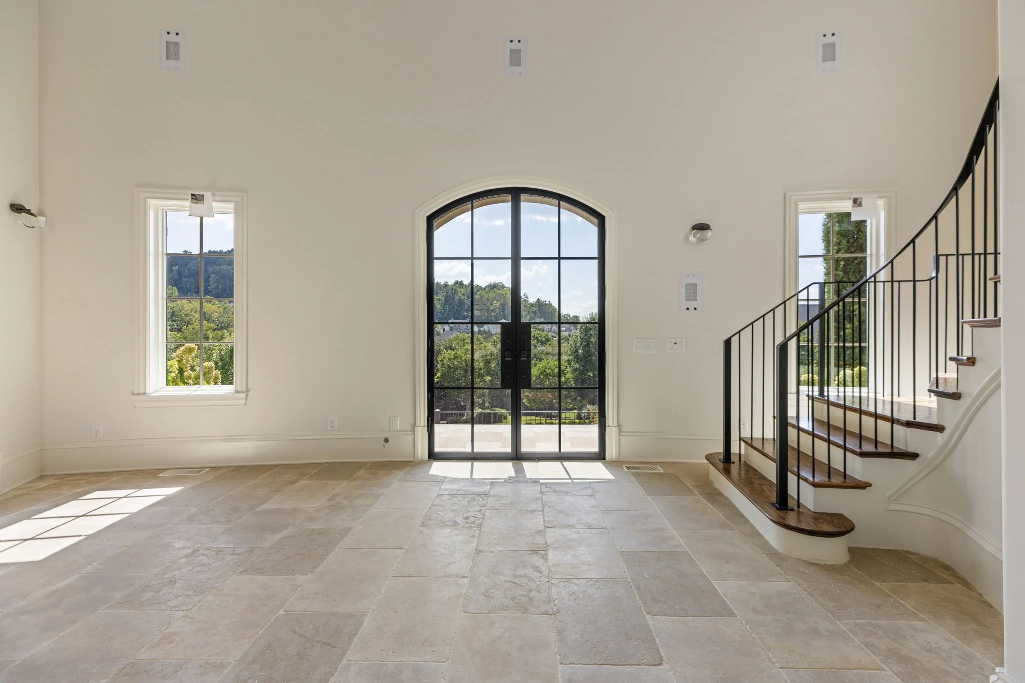 Empty room with large front door, two windows, a staircase, and natural light streaming in from the windows.
