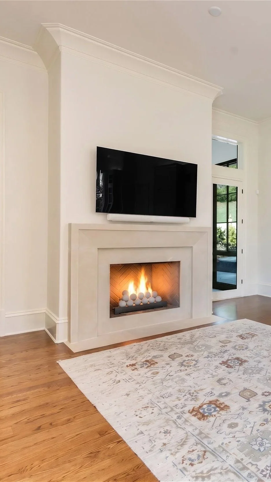 Kitchen with a fireplace, a wall-mounted flat-screen TV above it, and a sliding glass door in the background going to the sun room. The fireplace has decorative spheres and a fire burning.