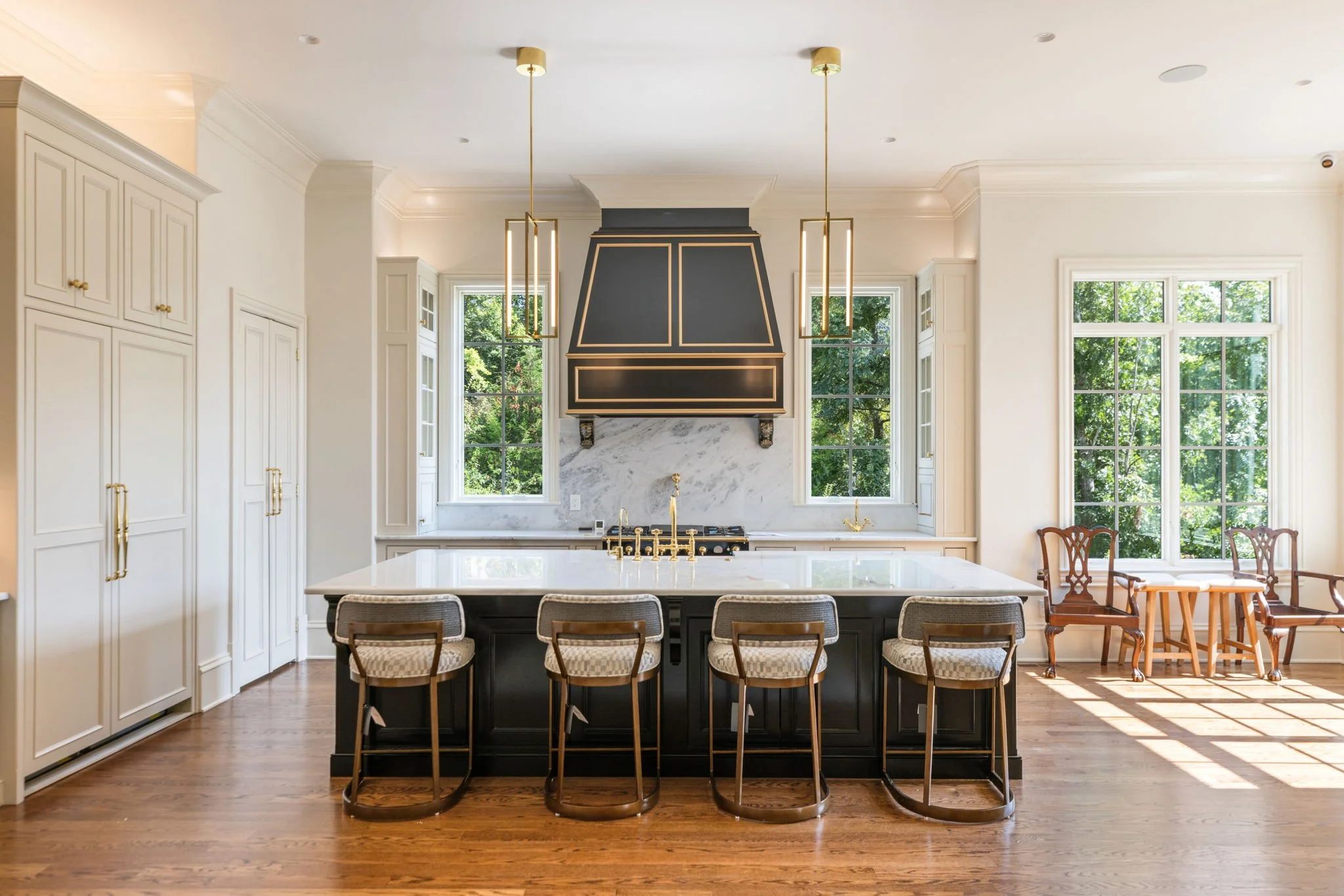 Modern kitchen with white cabinets, black island, marble backsplash, paneled appliances, and brass light fixtures hanging from the ceiling.