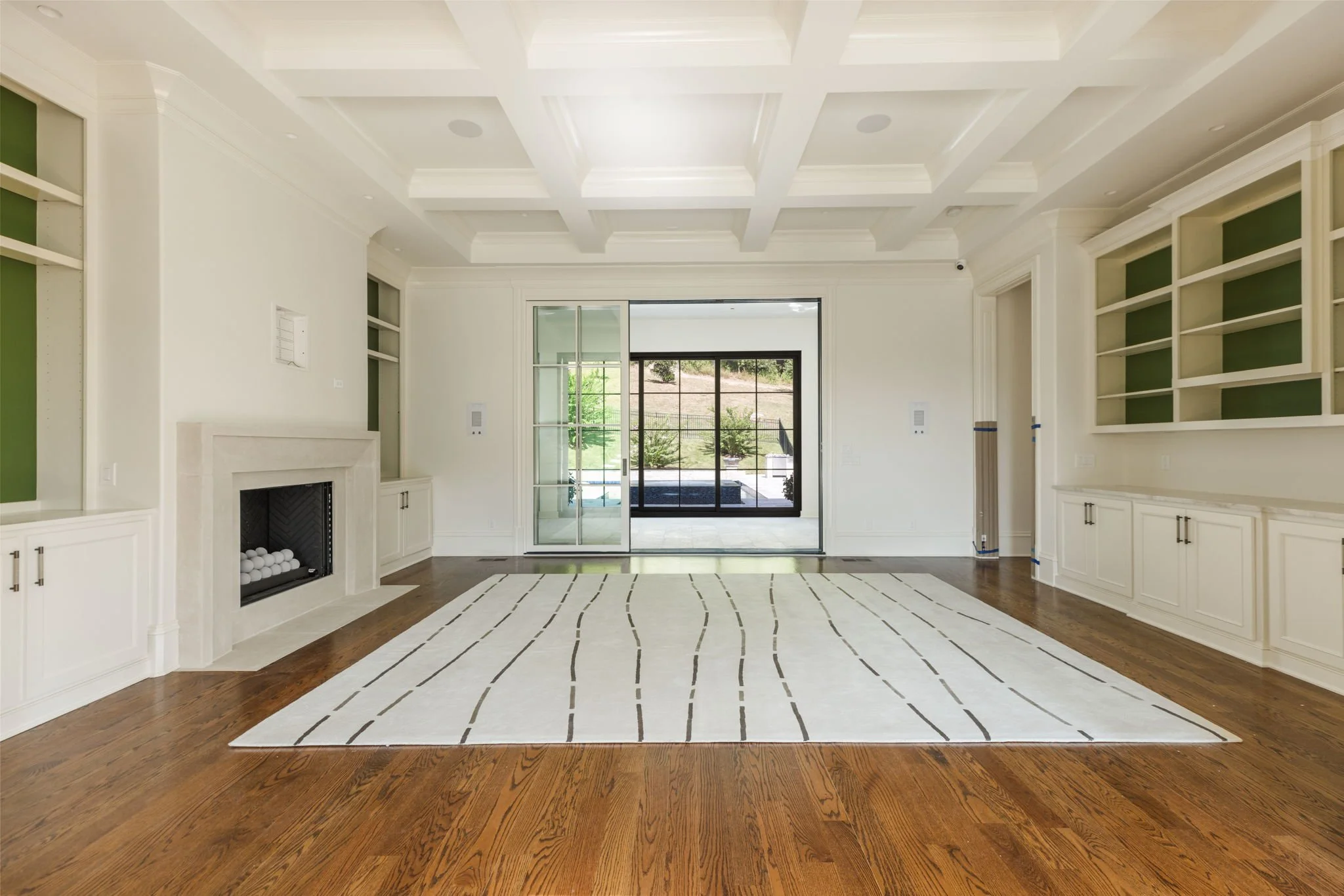 Empty living room with hardwood floors, white walls, built-in shelves, a fireplace, sliding glass doors, and a view of the sun room.