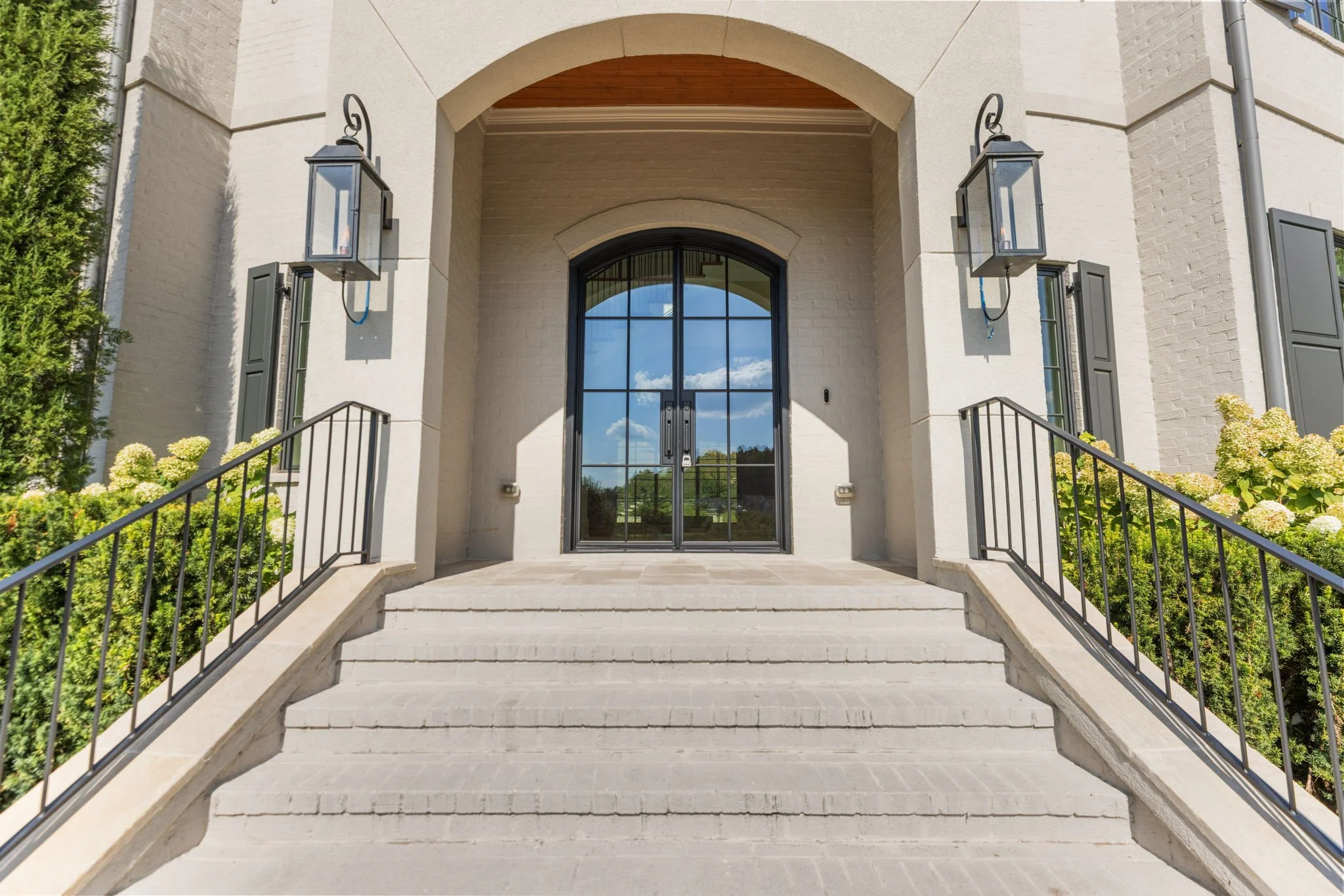 Front entrance of a house with stairs leading up to a glass door, black metal railings, and two large wall-mounted lanterns on either side.