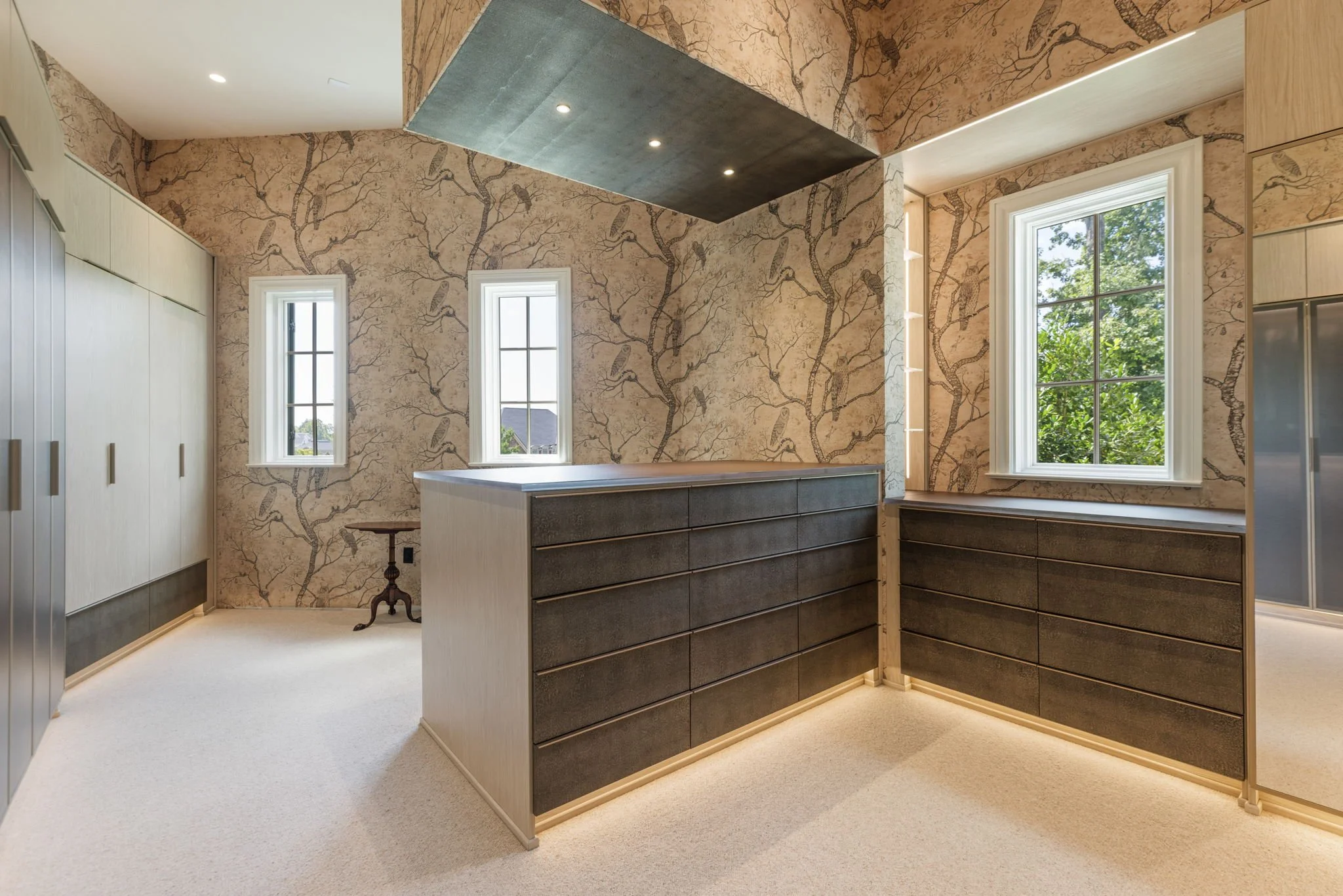 Interior of a custom, California Closet's closet with wallpaper, built-in cabinetry, and a floating ceiling with recessed pen lights.