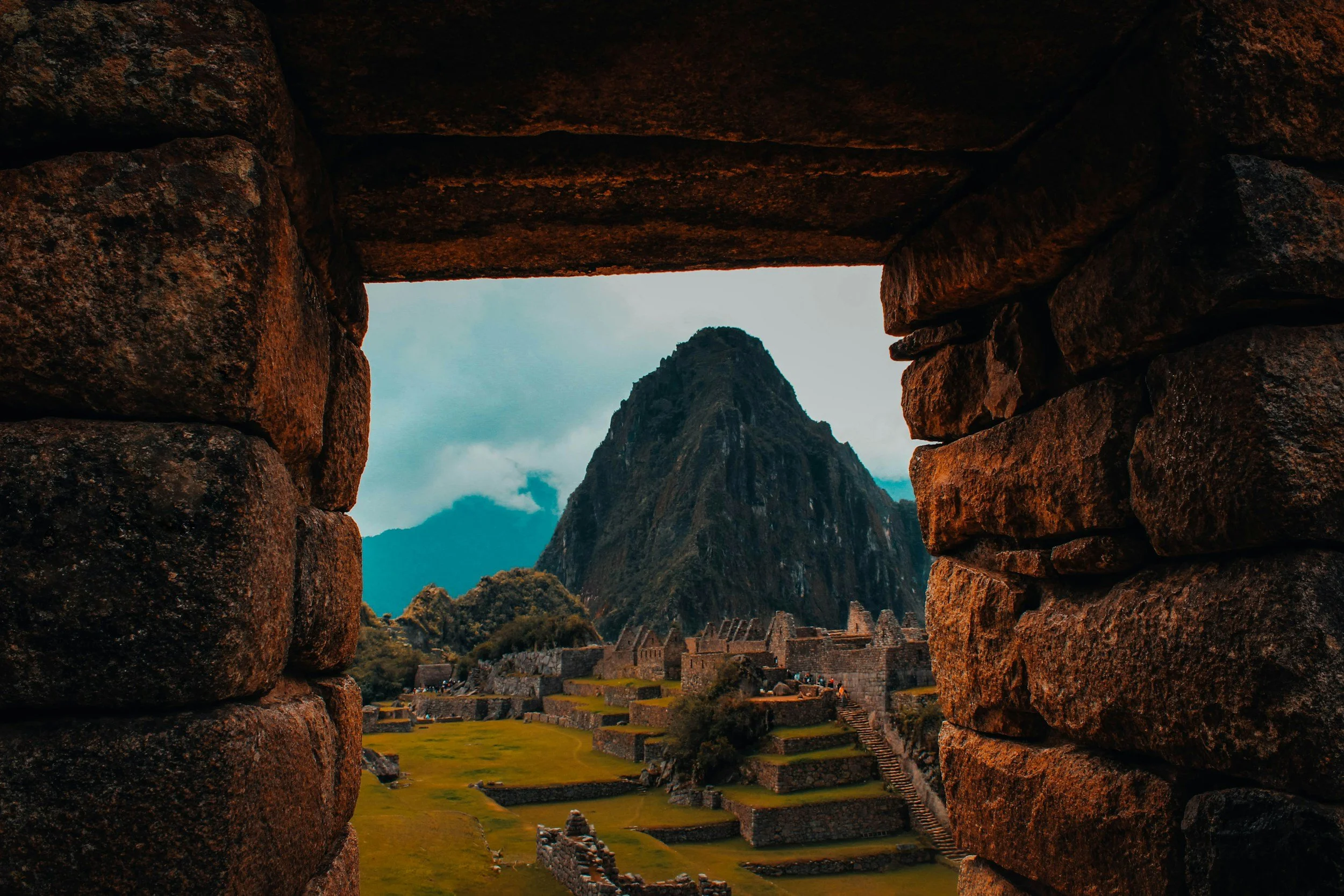 View of Machu Picchu through stone window framing, with the iconic mountain Huayna Picchu in the background.