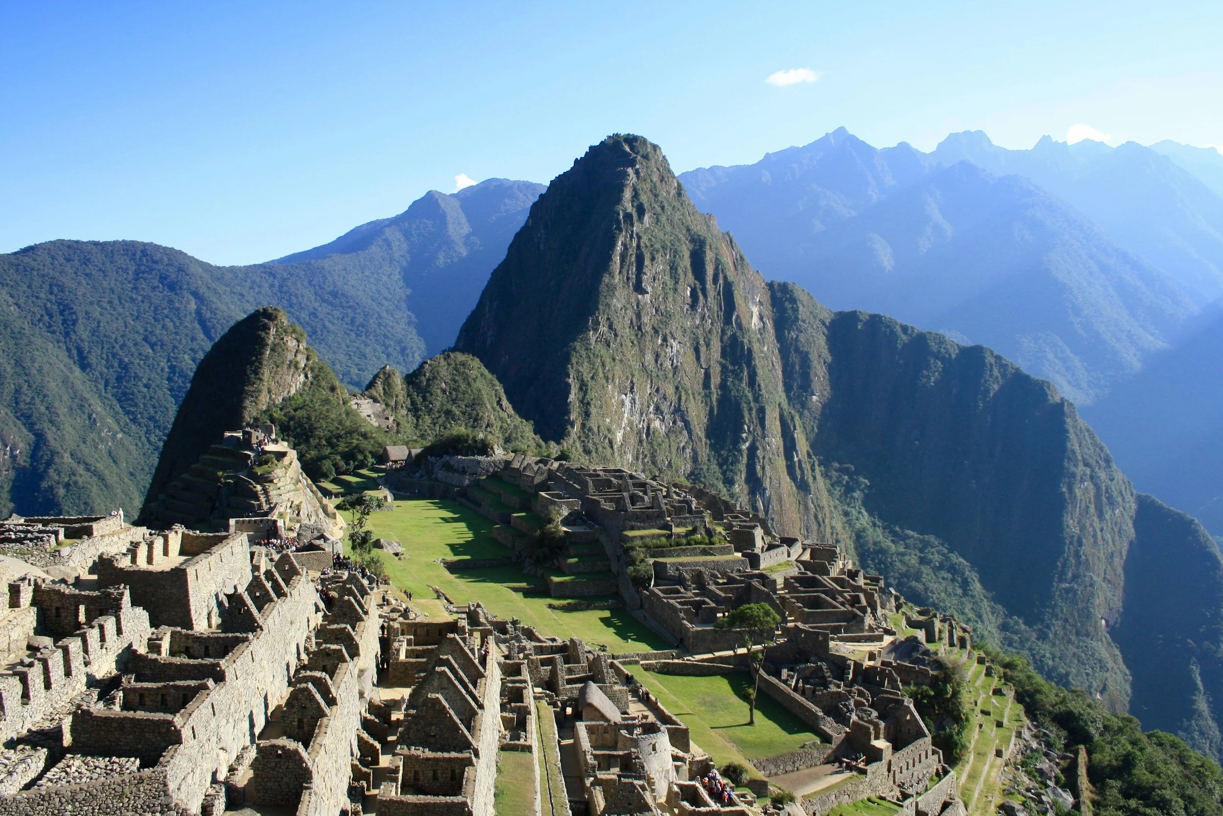 Ancient Incan ruins of Machu Picchu surrounded by lush green mountains under a bright blue sky.