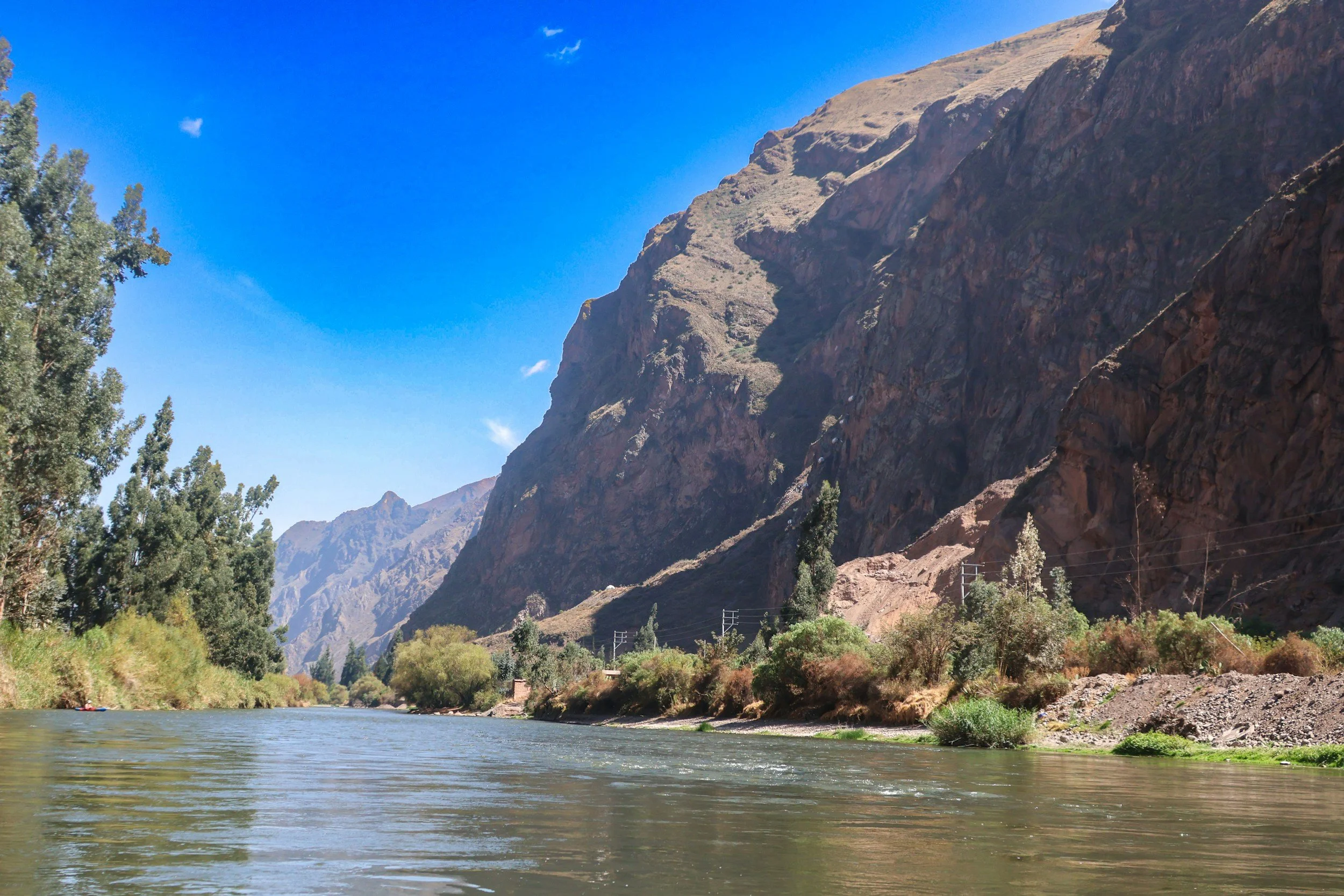 Scenic view of a river flowing through a valley surrounded by towering rocky mountains under a clear blue sky.
